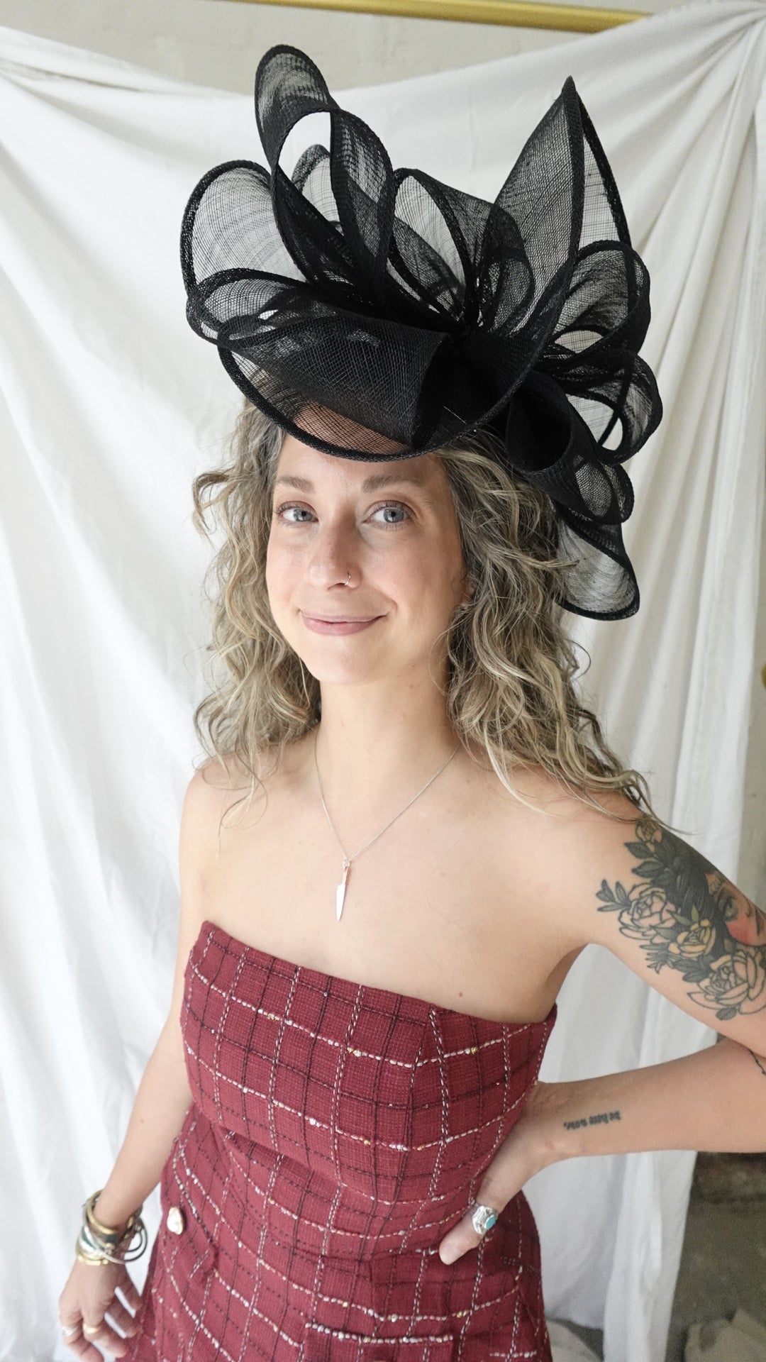 Woman wearing a large black feathered hat and a red checkered dress on a white background