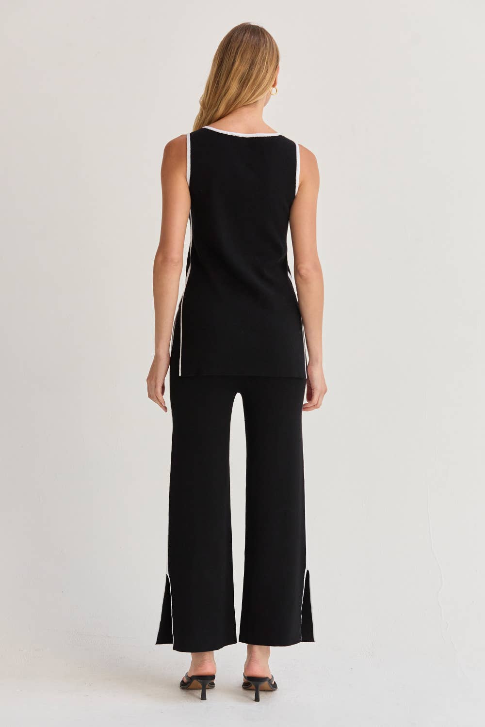 Woman wearing a black sleeveless top and wide-leg pants on a plain background