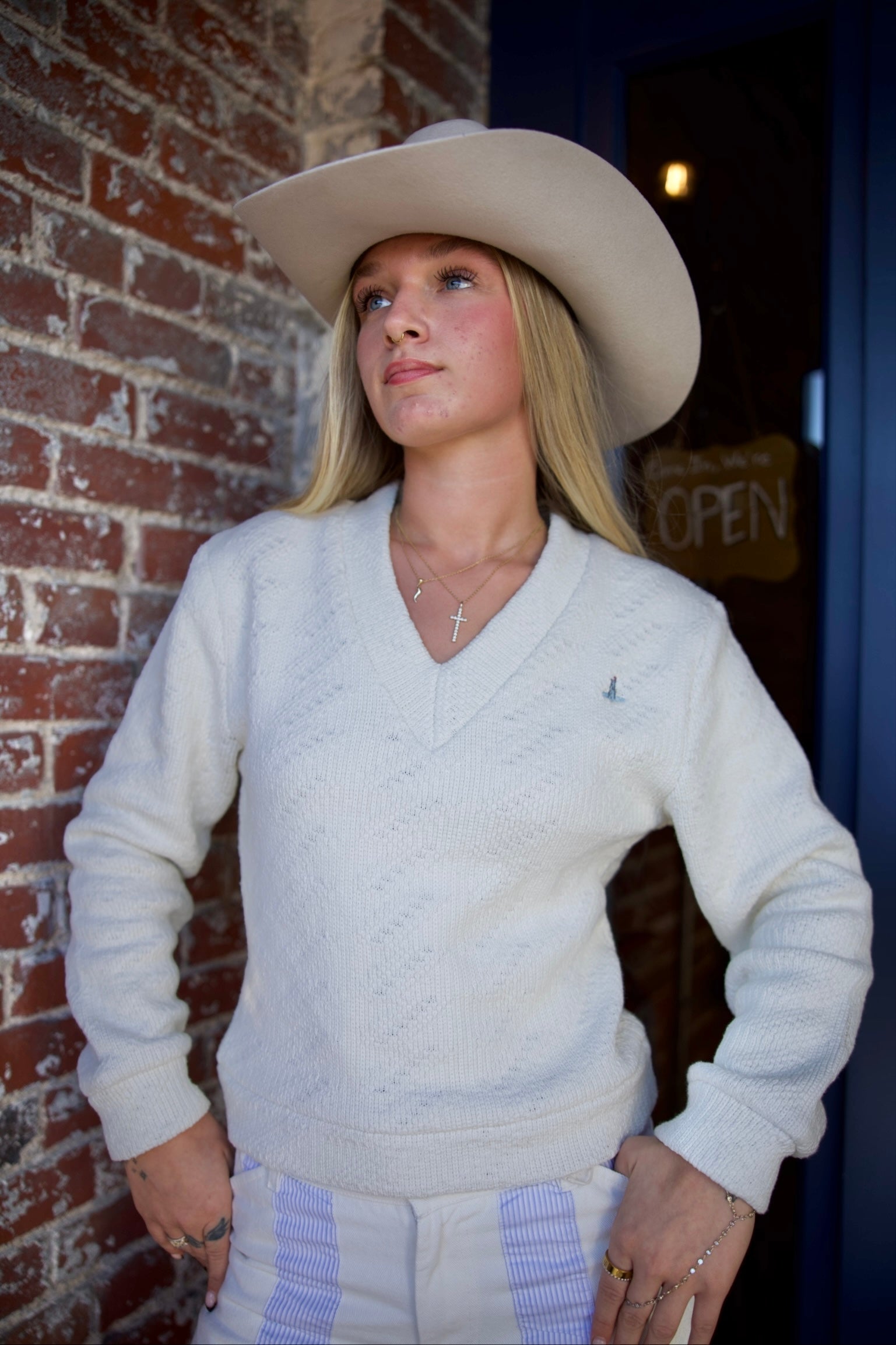 Woman wearing a white sweater and cowboy hat against a brick wall.
