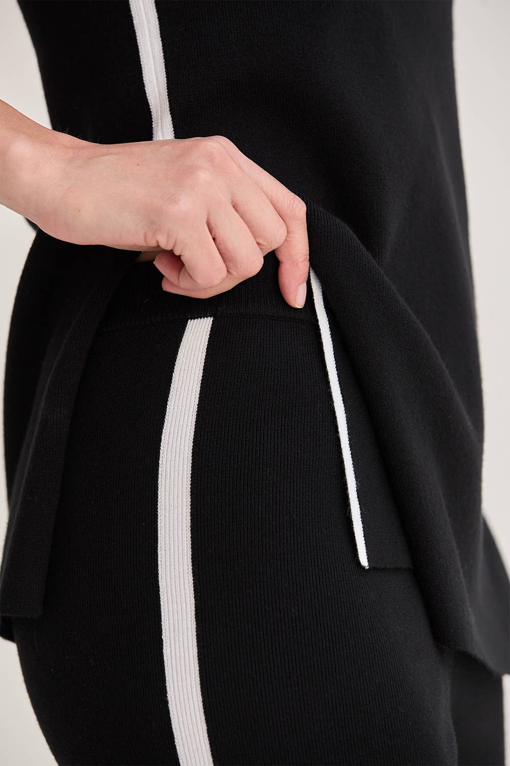 Black outfit with white stripes being adjusted by a person on a light gray background