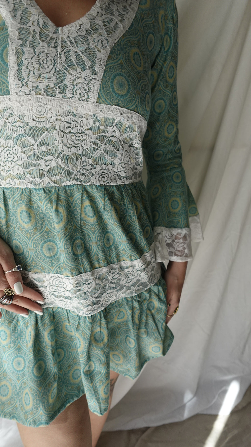 Green patterned fabric with lace details held by a person.