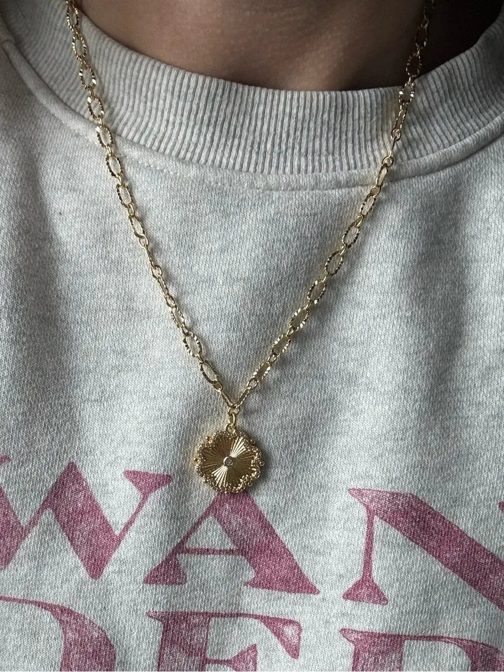 Gold necklace with a pendant on a gray sweatshirt with pink text