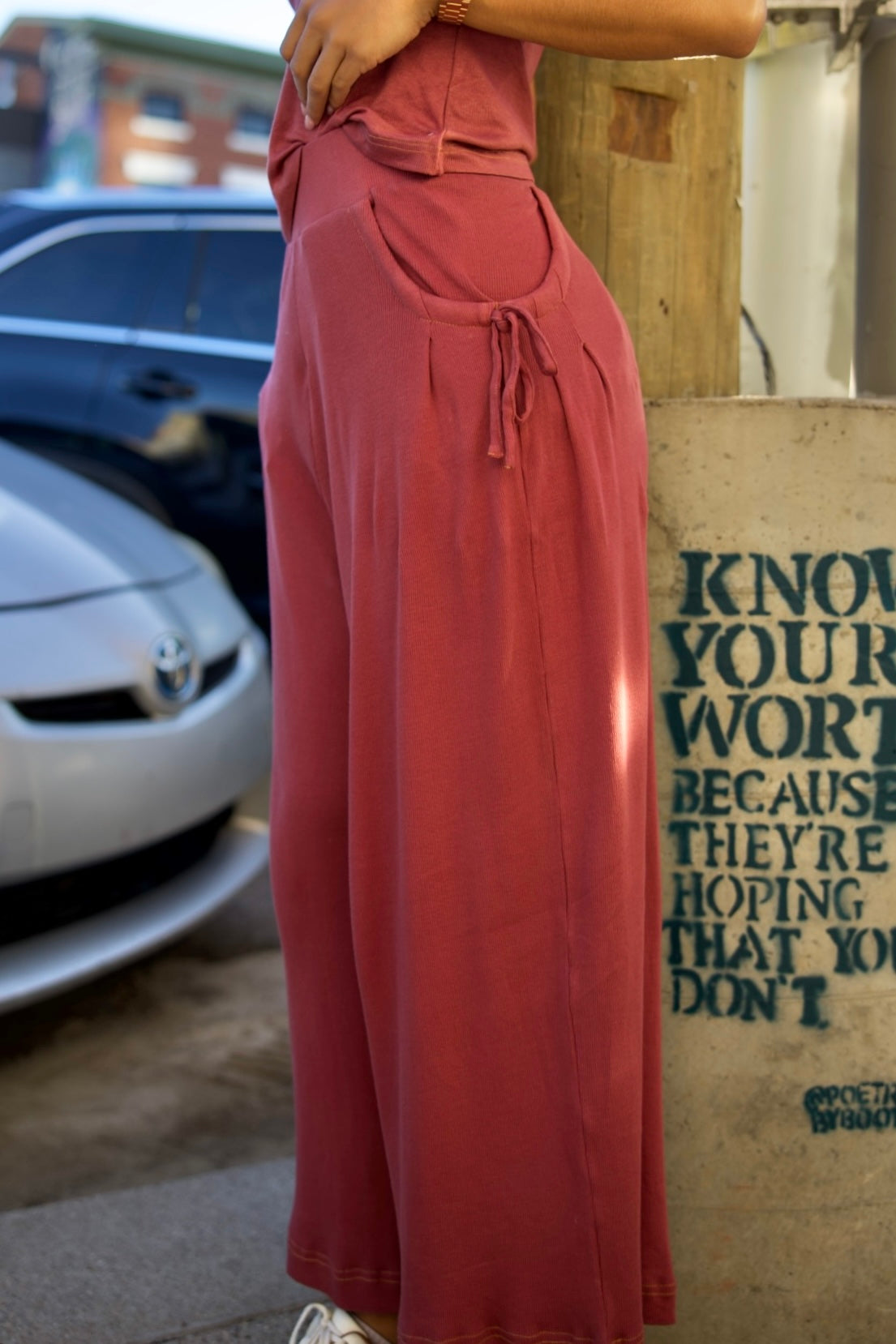 Person wearing a long rust-colored dress standing next to a wall with text.