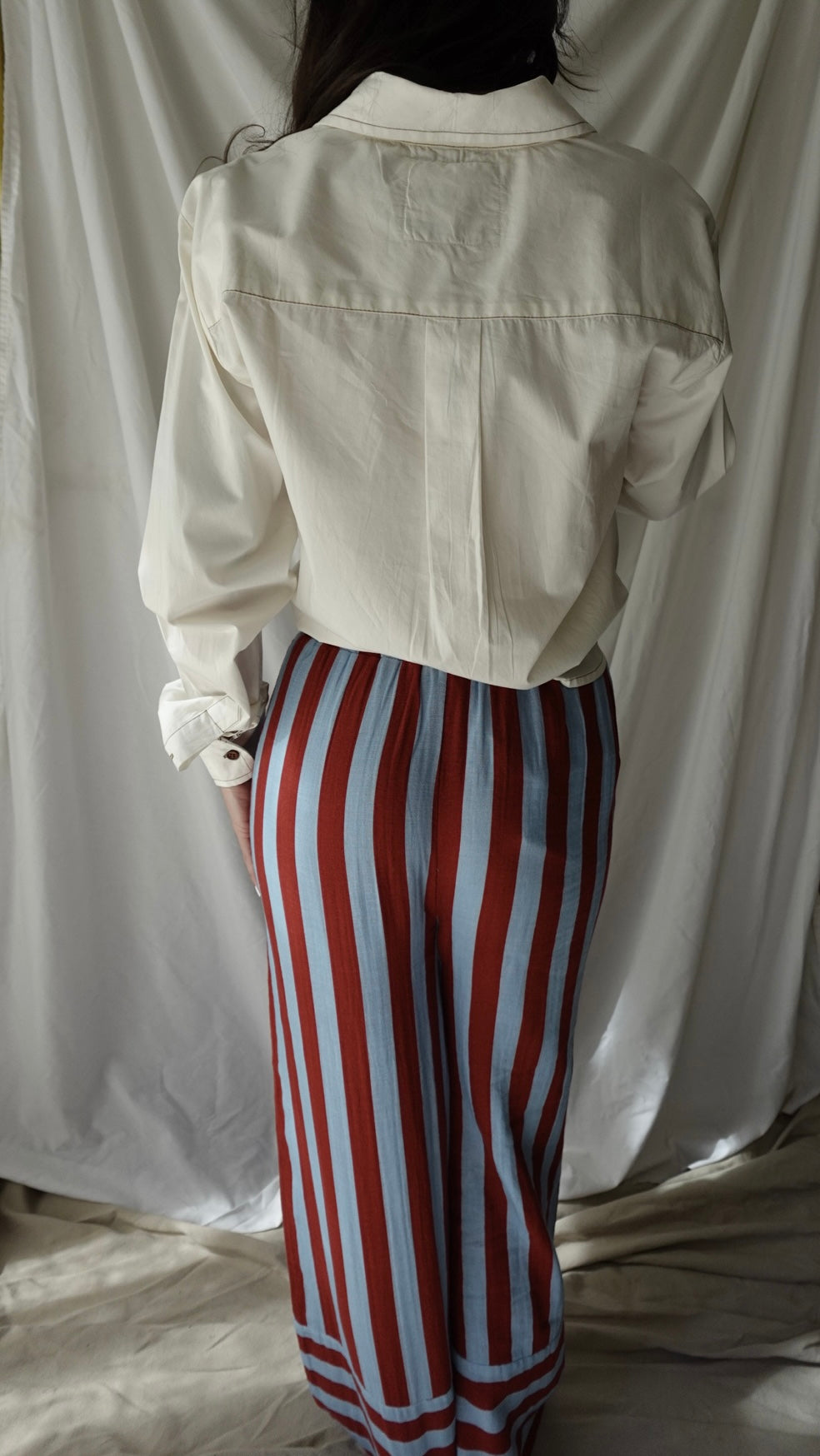 Person wearing a beige jacket and red and white striped pants against a plain background