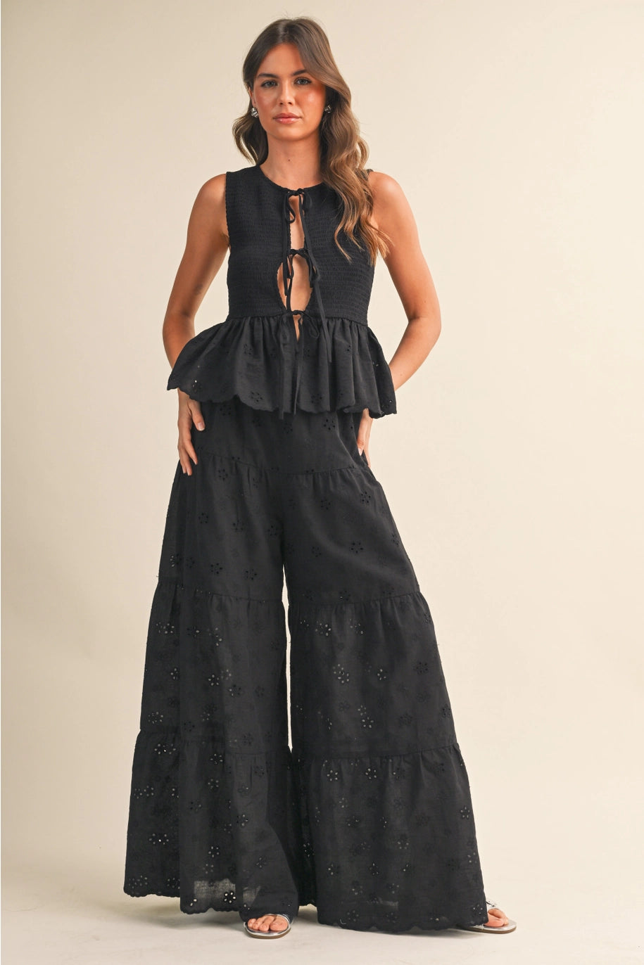 Woman wearing a black peplum top and wide-leg pants on a beige background