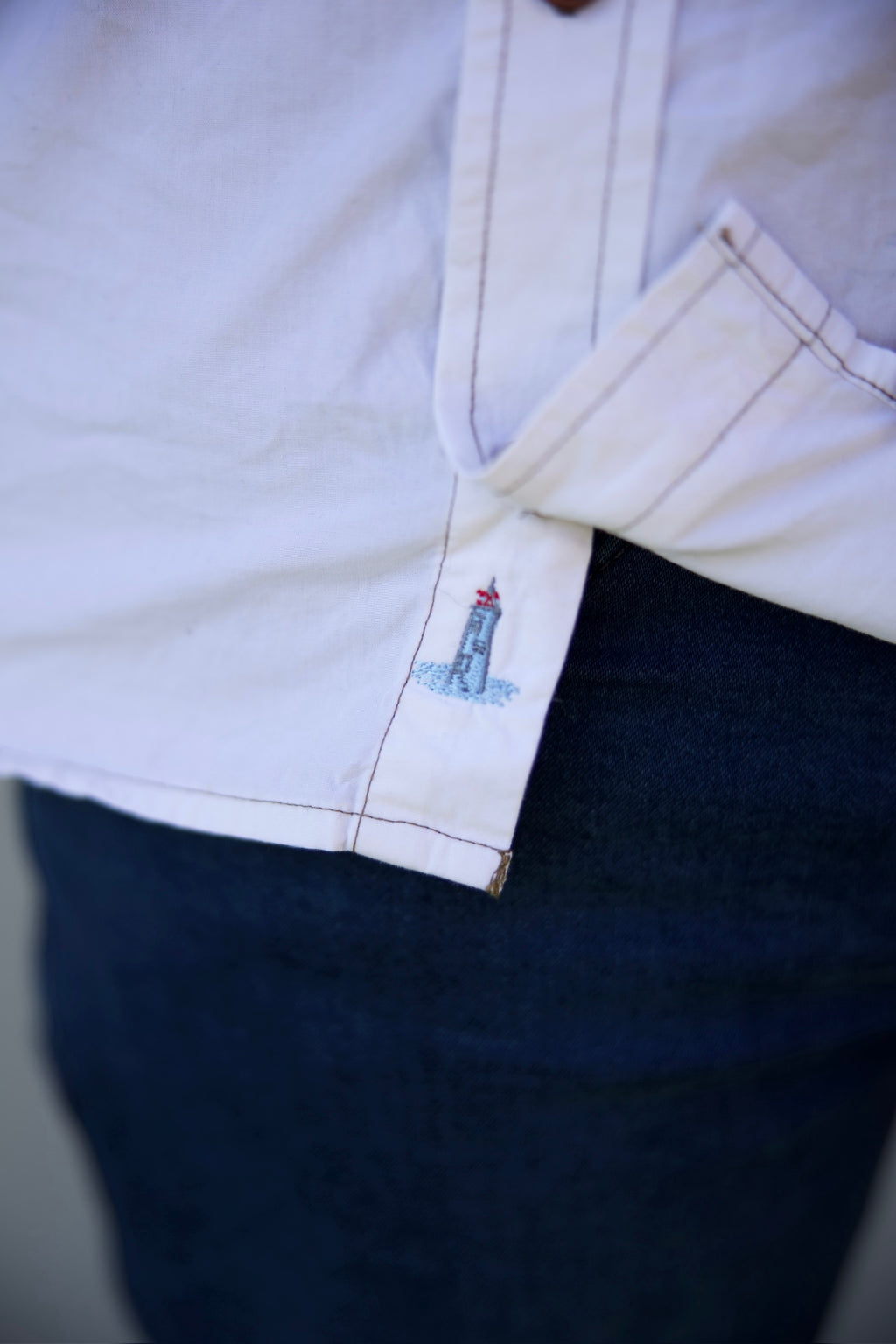 Close-up of a white shirt with a lighthouse design on the collar, worn with dark pants.