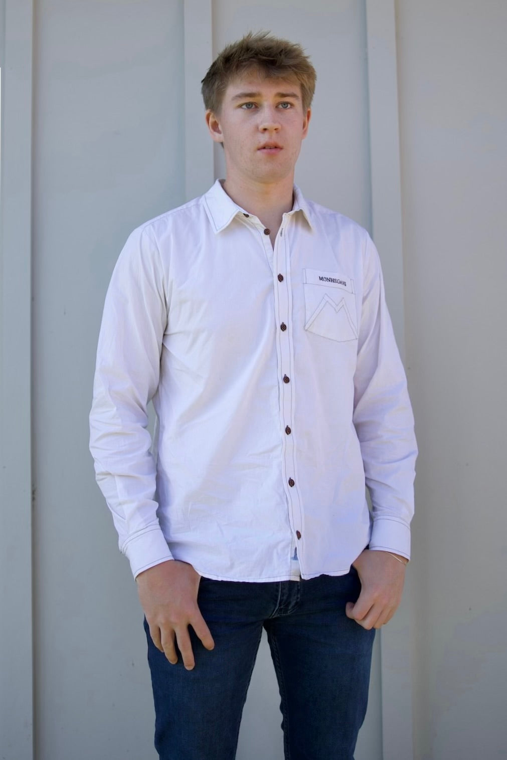 Person wearing a light-colored button-up shirt and dark jeans against a plain background