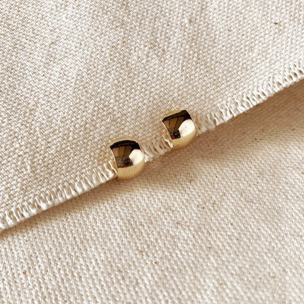 Gold hexagonal earrings on a textured beige fabric background
