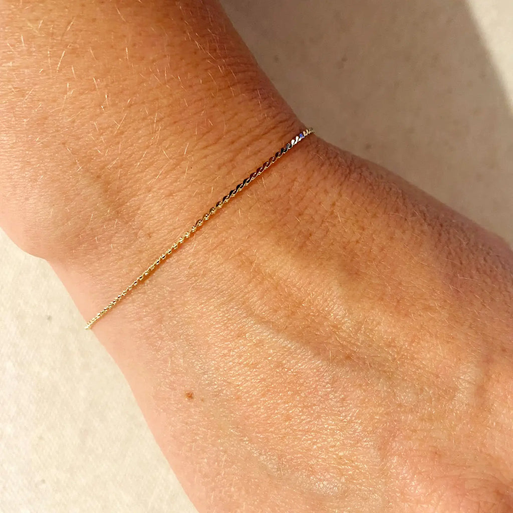 Gold anklet on a person's ankle against a neutral background