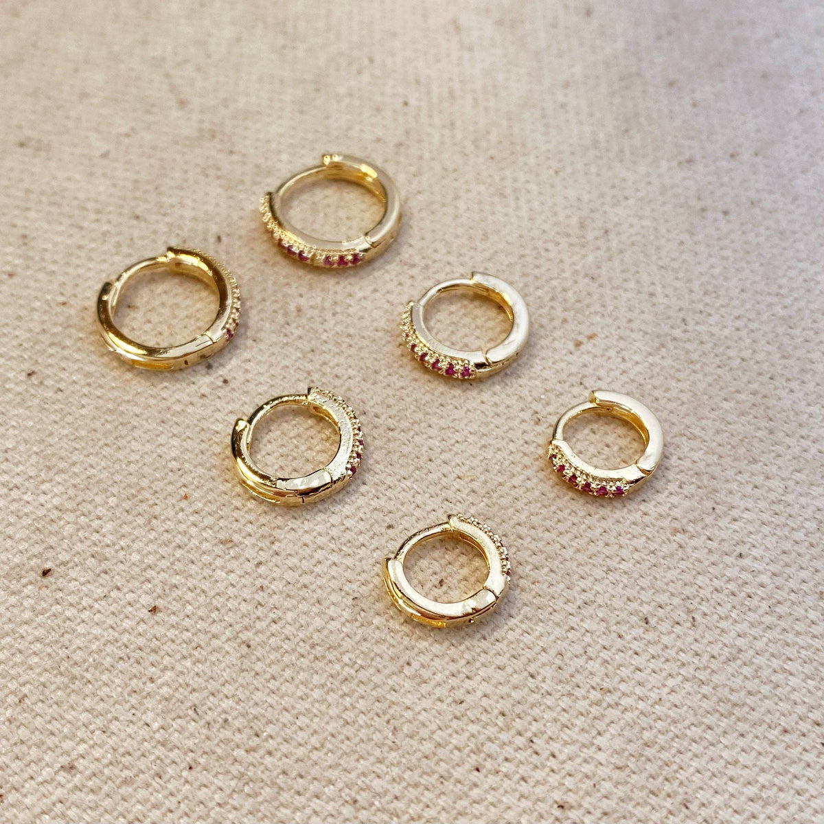 Gold hoop earrings with red gemstones on a beige fabric background