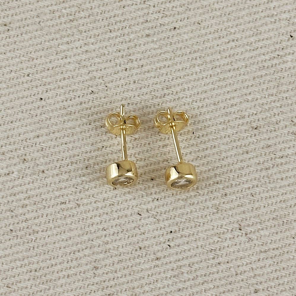 Gold stud earrings on a textured beige background