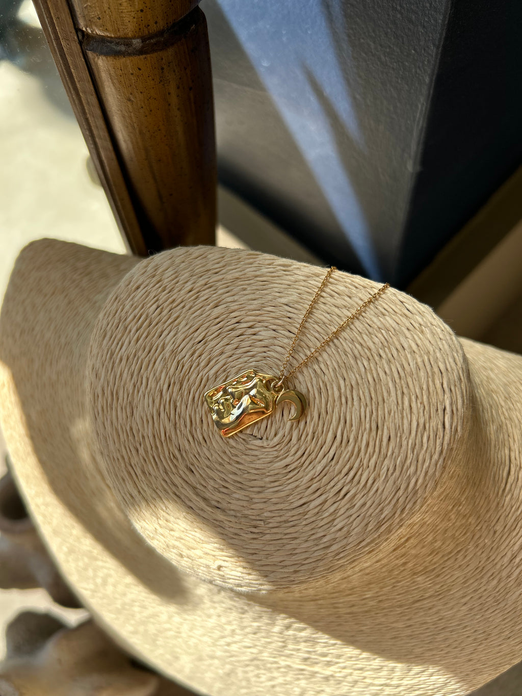 Gold necklace with a pendant draped over a straw hat