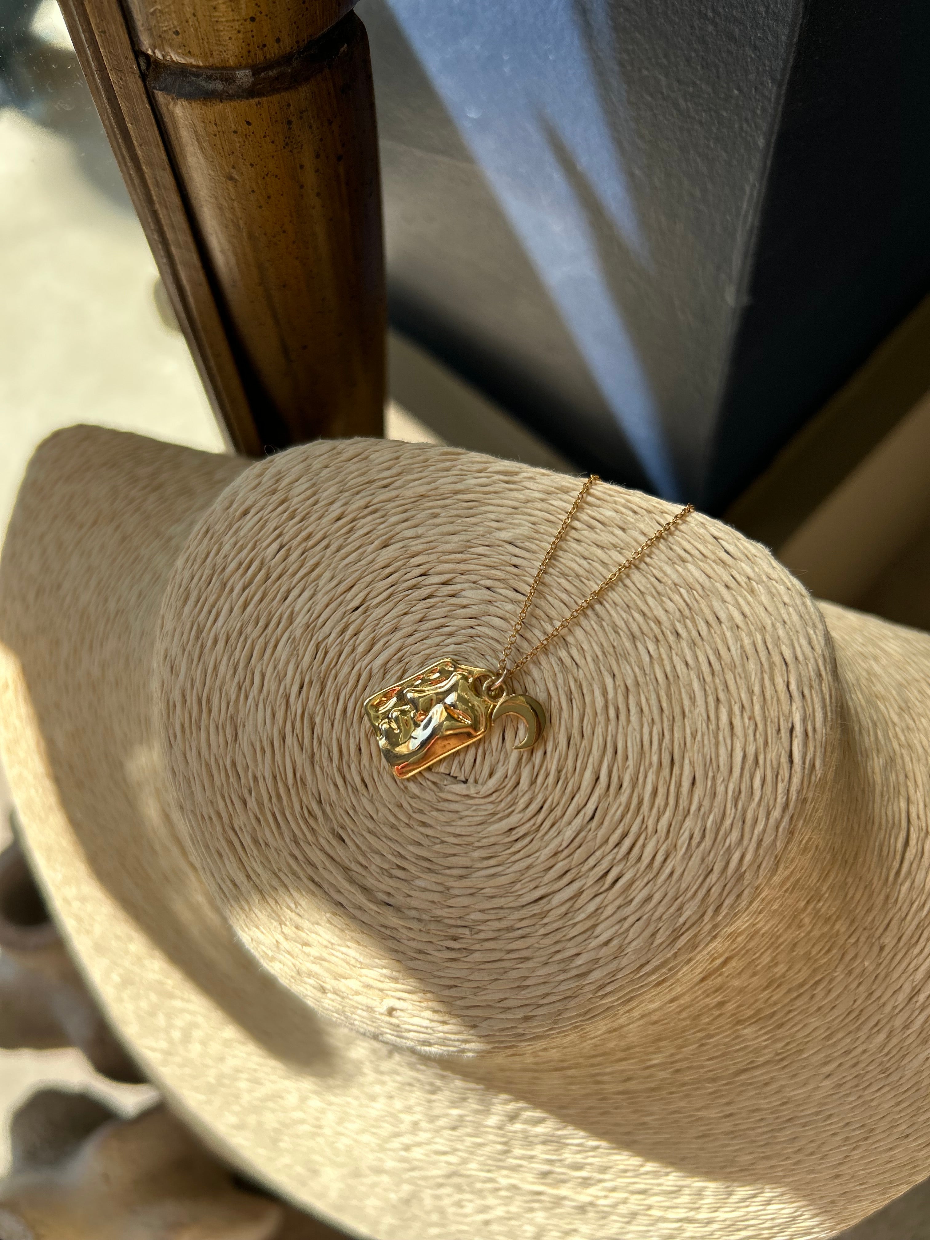 Gold necklace with a pendant draped over a straw hat
