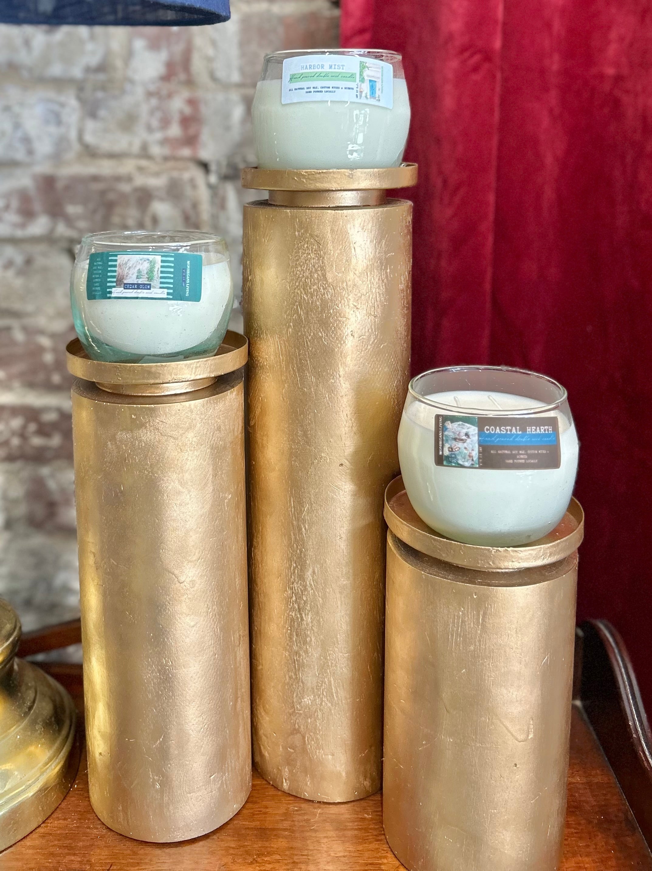 Candle holders with candles on a wooden surface against a brick wall.