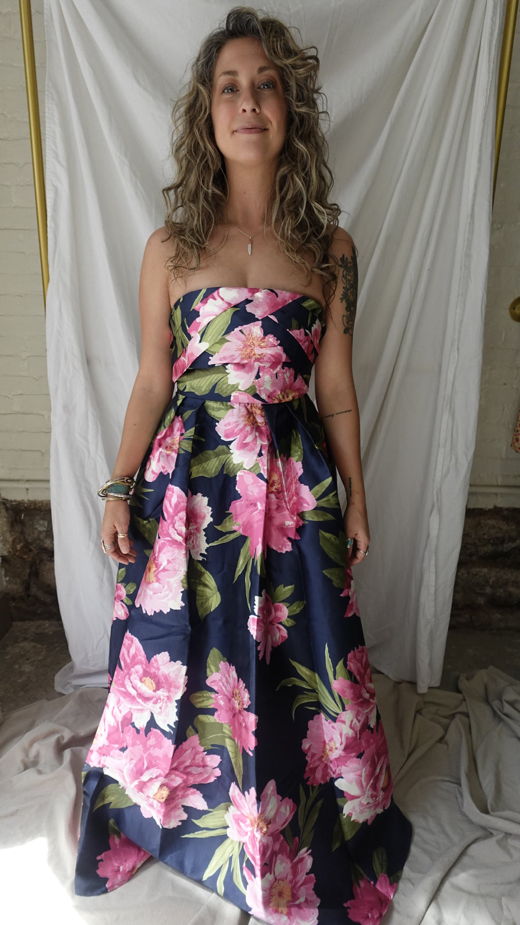 Woman wearing a floral dress standing against a white curtain.