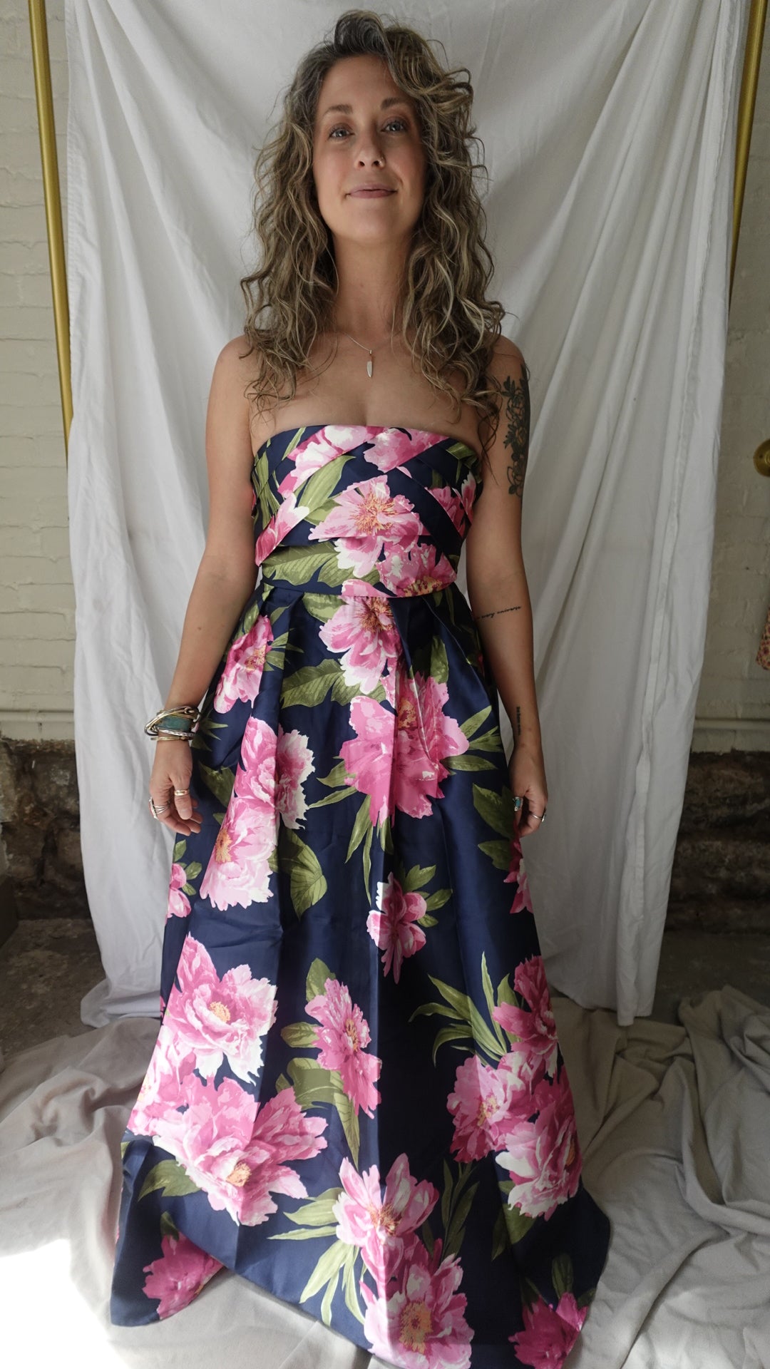 Woman wearing a floral dress standing against a white curtain.
