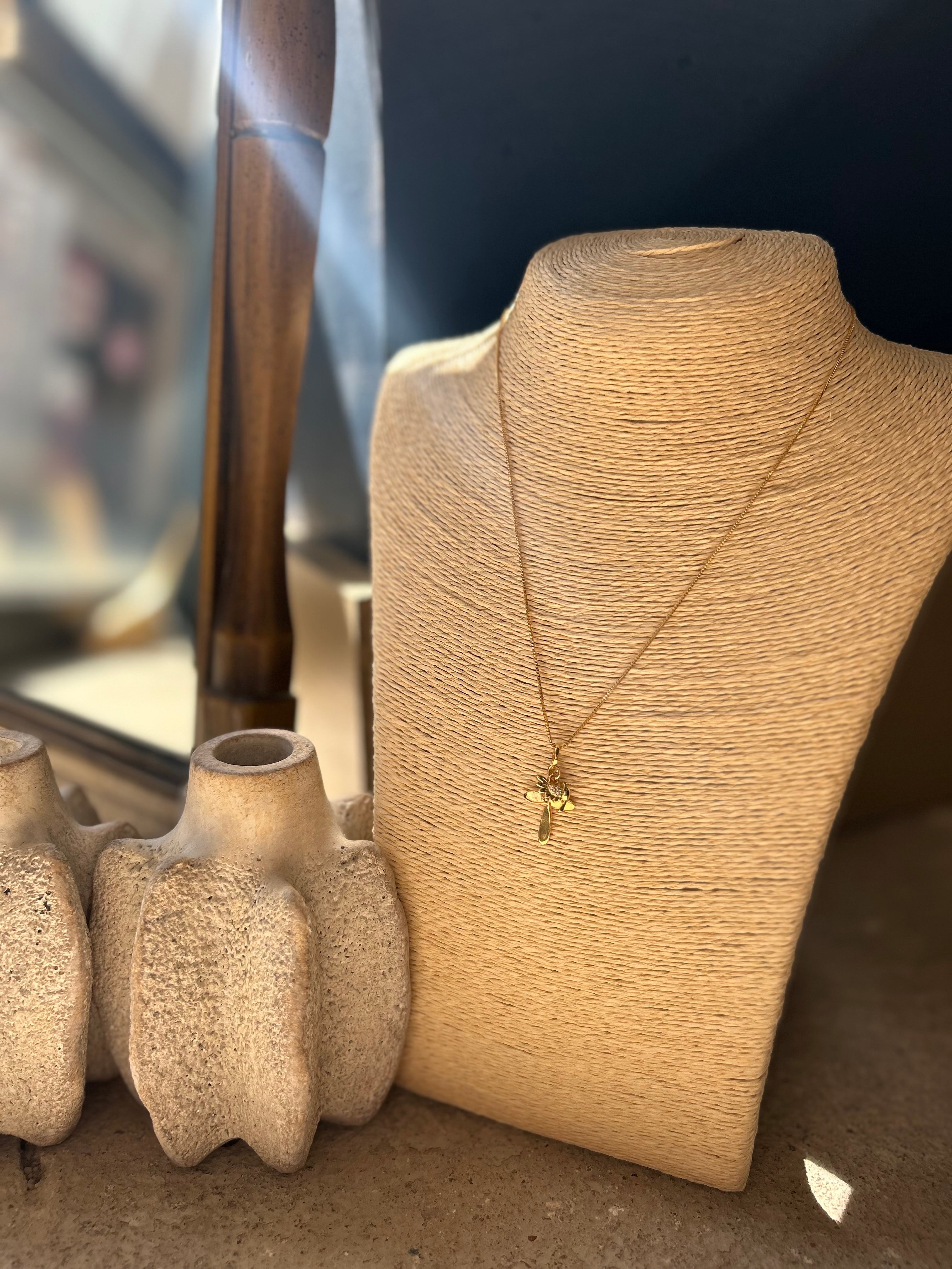 Gold necklace on a mannequin bust with textured vases in the background