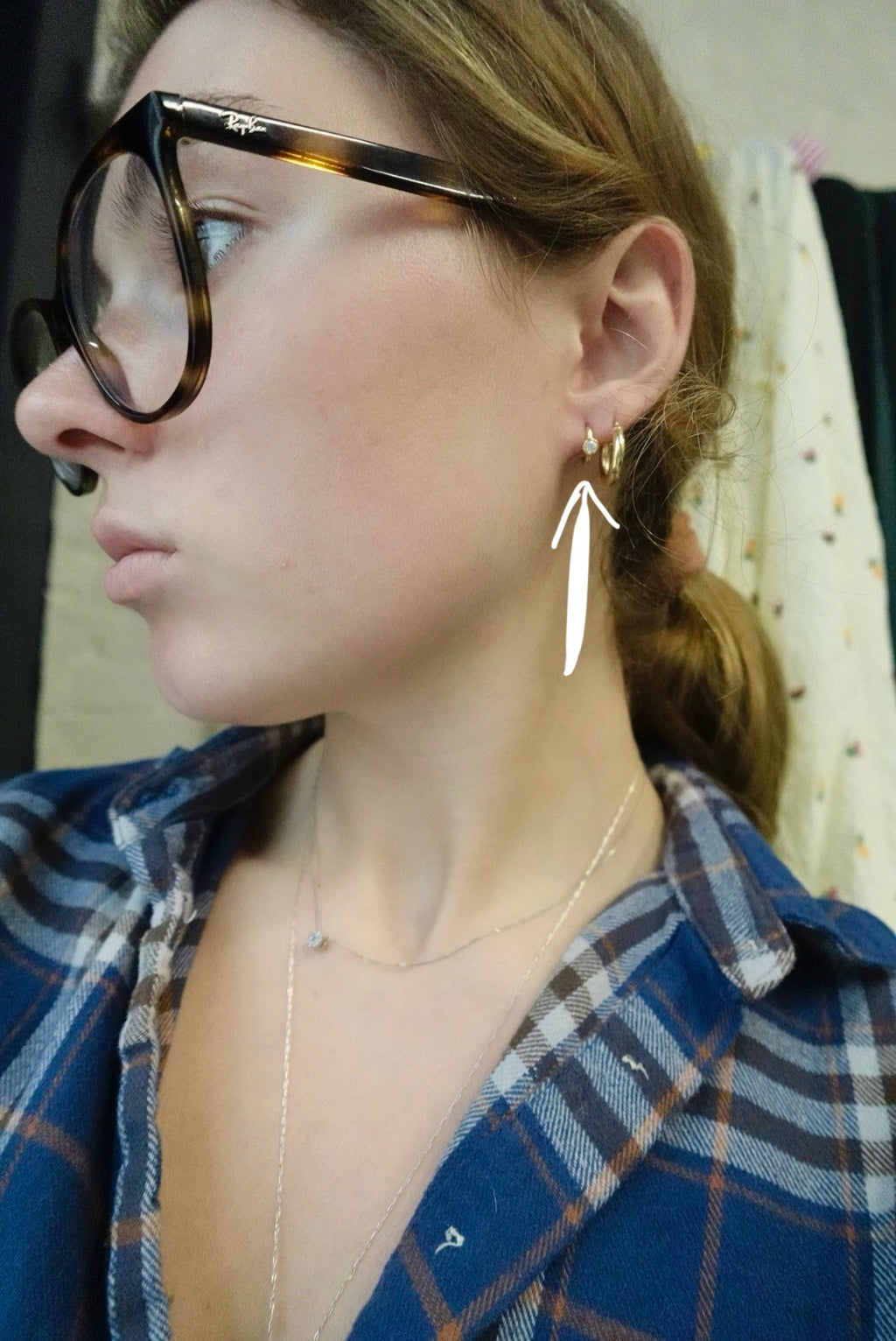 Person wearing a blue plaid shirt with a close-up of an earring.