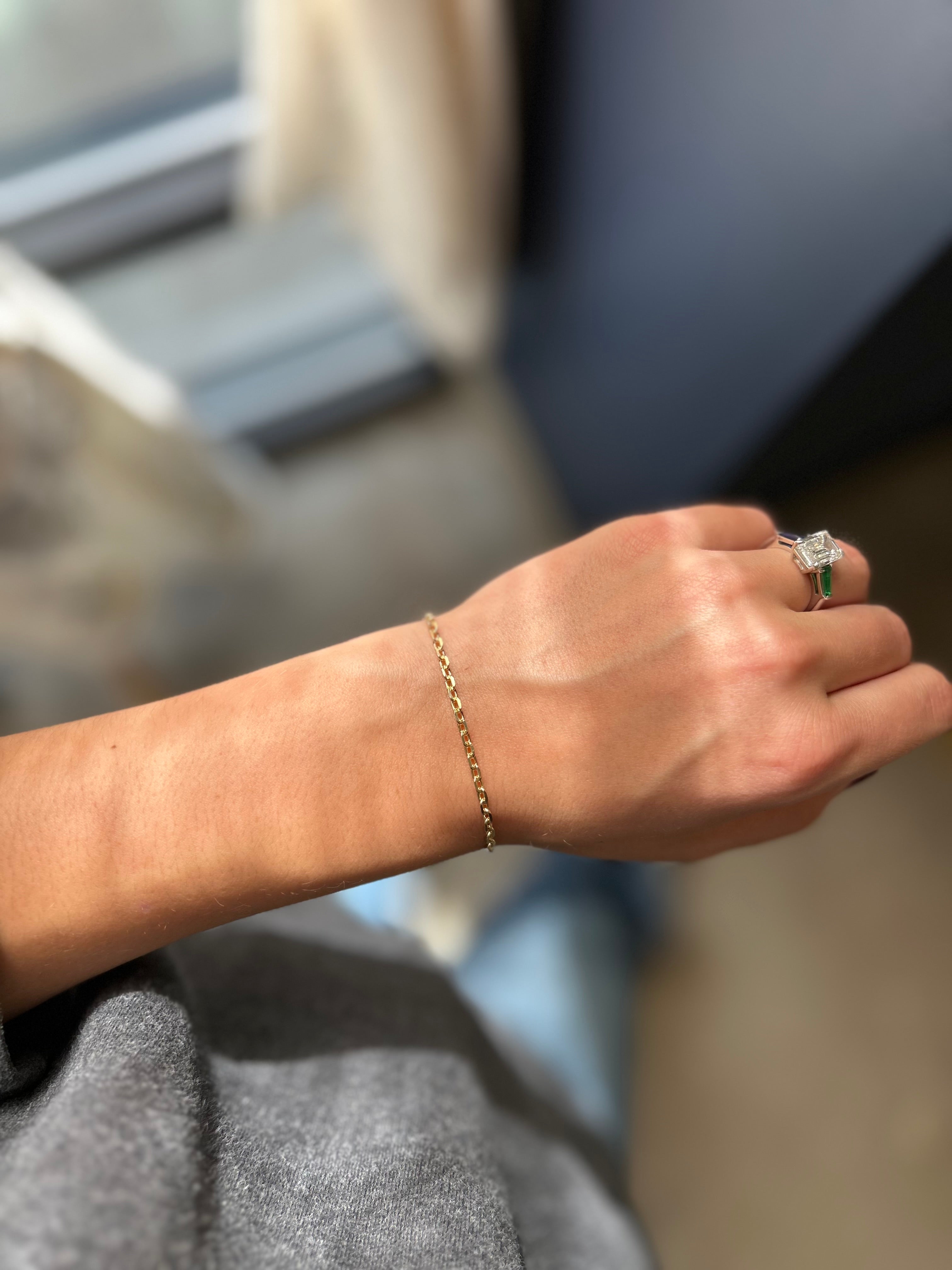 Hand wearing a gold bracelet and ring with a green stone, blurred background