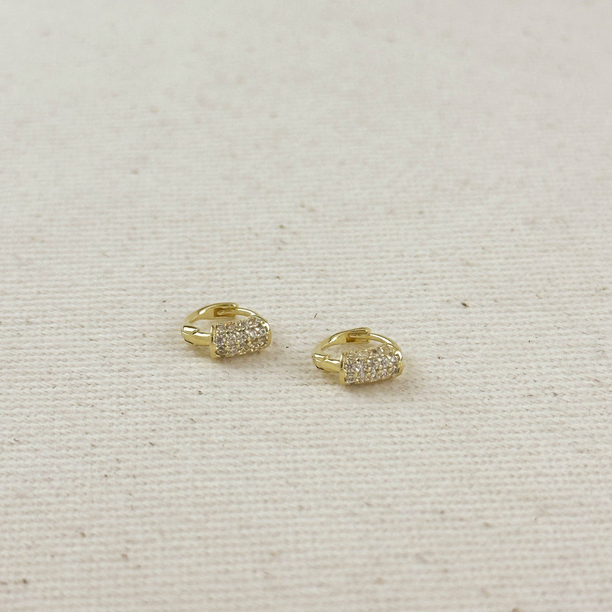Gold hoop earrings with embedded stones on a beige fabric background