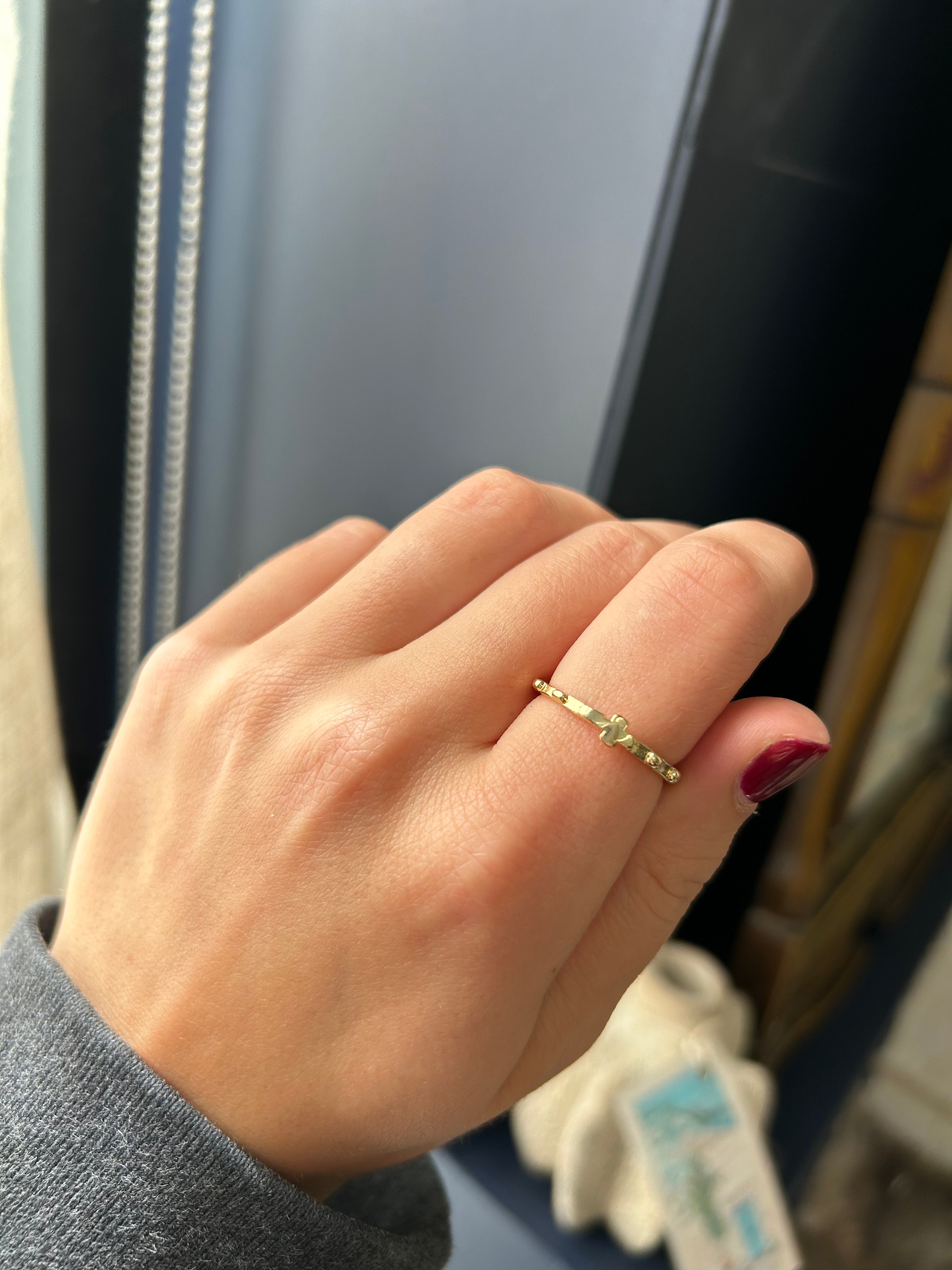Hand wearing a gold ring with a green gemstone, blurred background