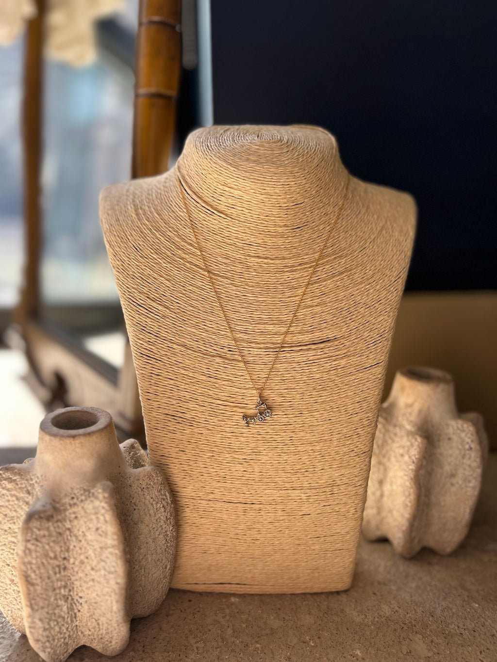 Necklace on a textured mannequin bust with decorative vases in the background