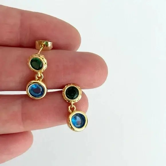 Gold earrings with colored stones held between fingers on a white background