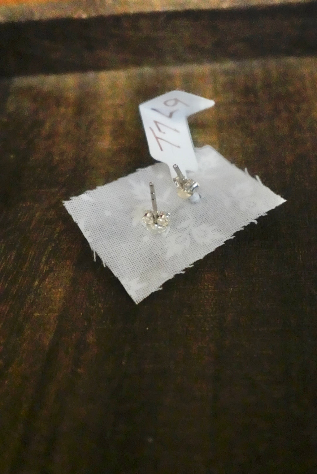 Pair of silver earrings on a white card with a brown background