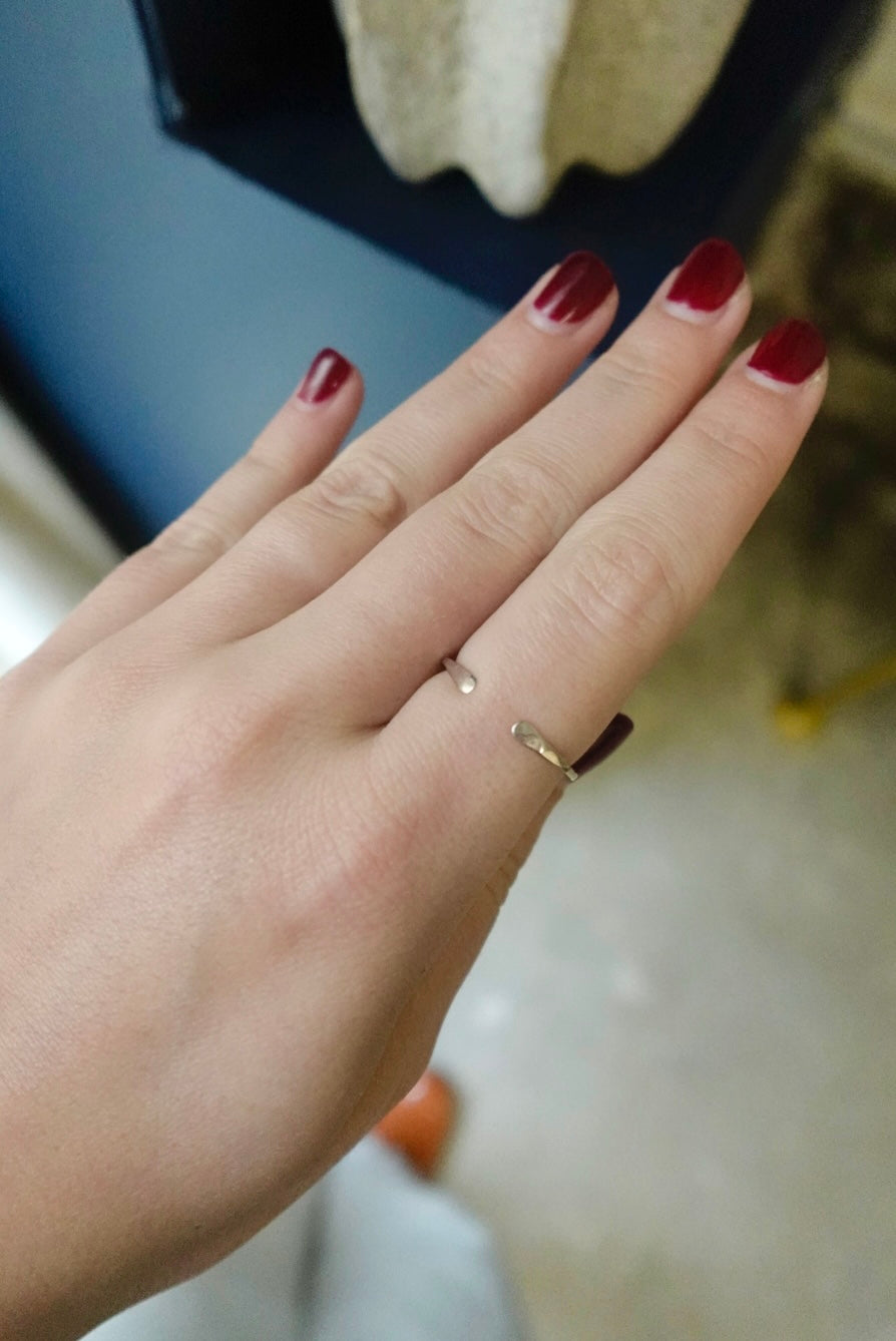 Hand with red nail polish wearing a gold ring on a blurred background