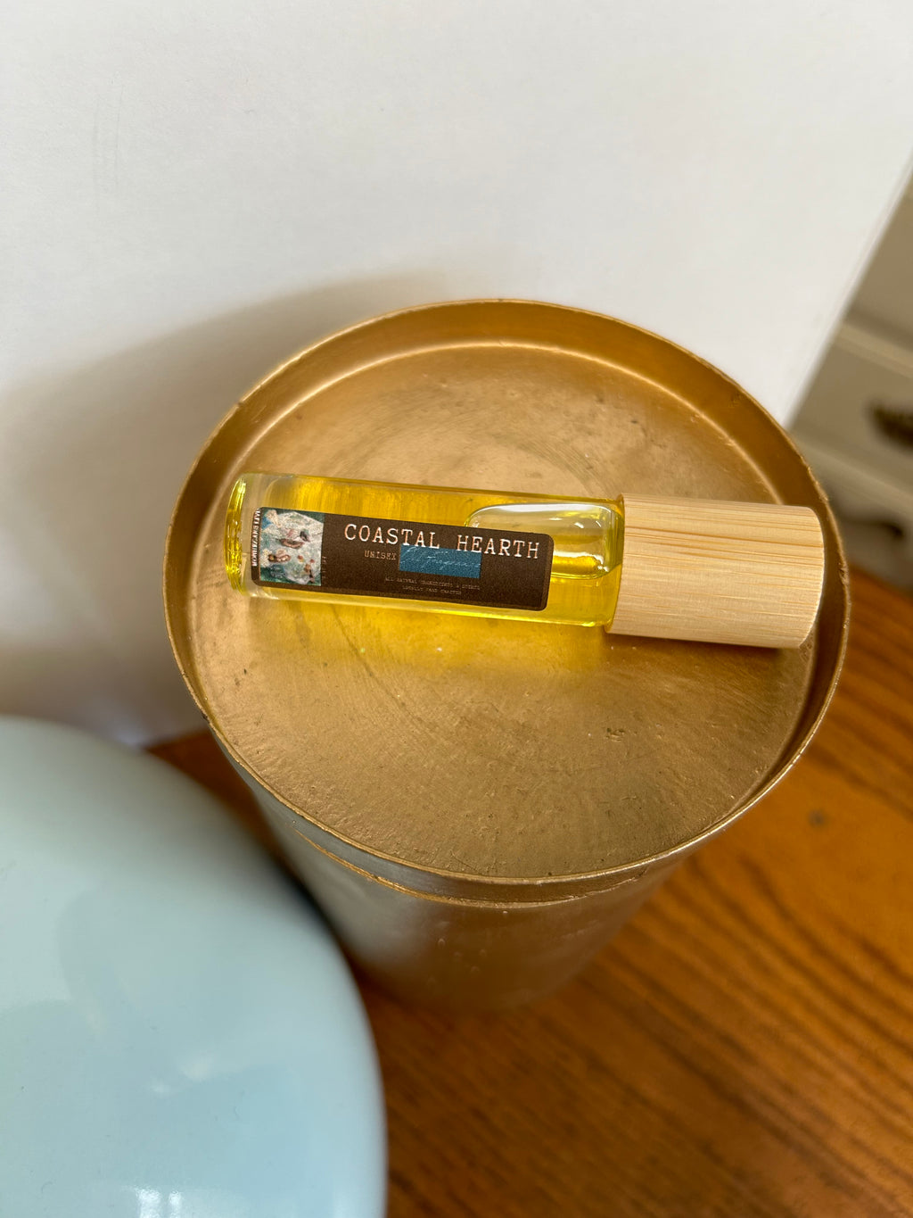 Small bottle of perfume with wooden cap inside a gold container on a white surface.