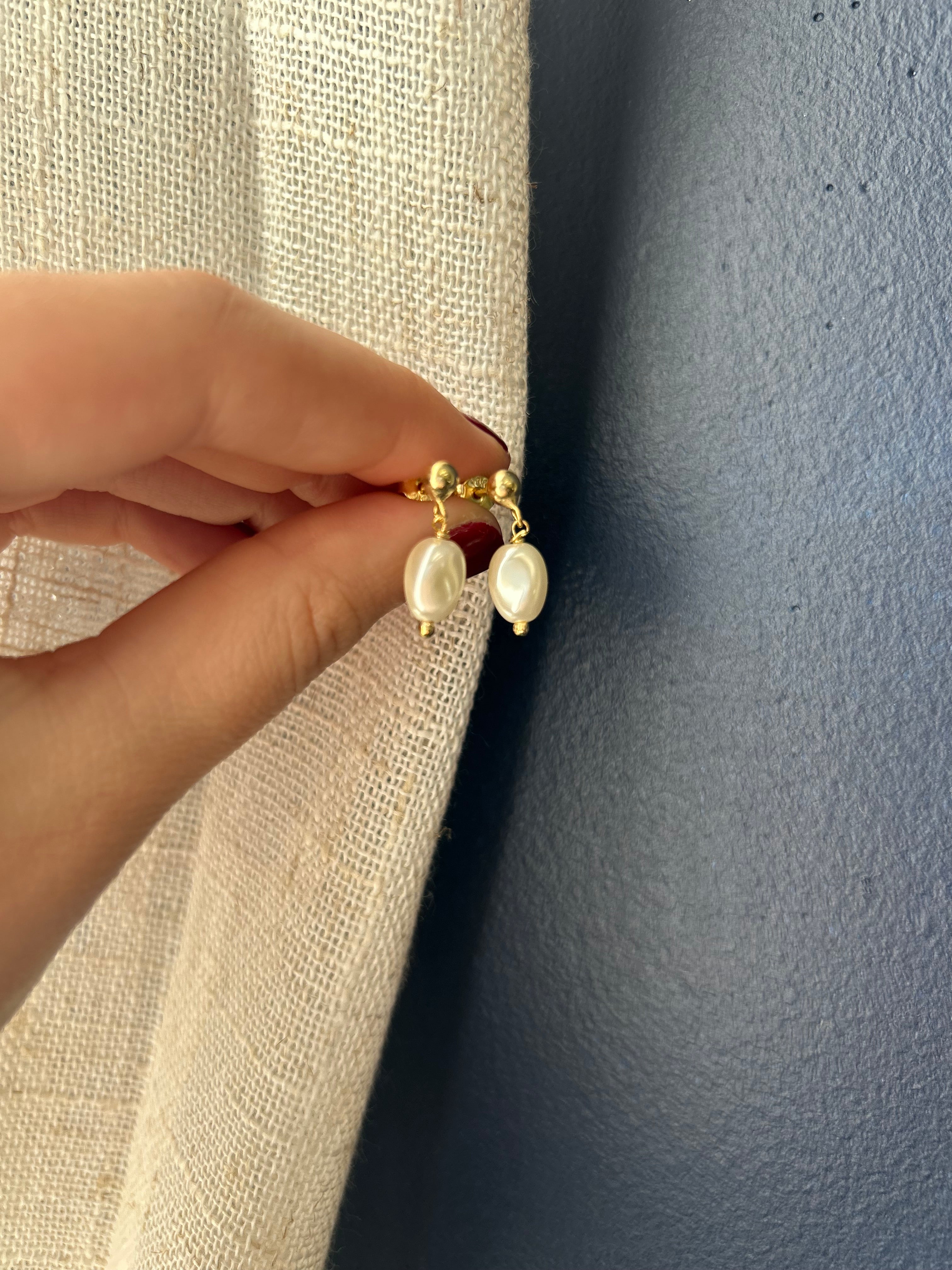 Gold earring with pearls held by a hand against a textured surface
