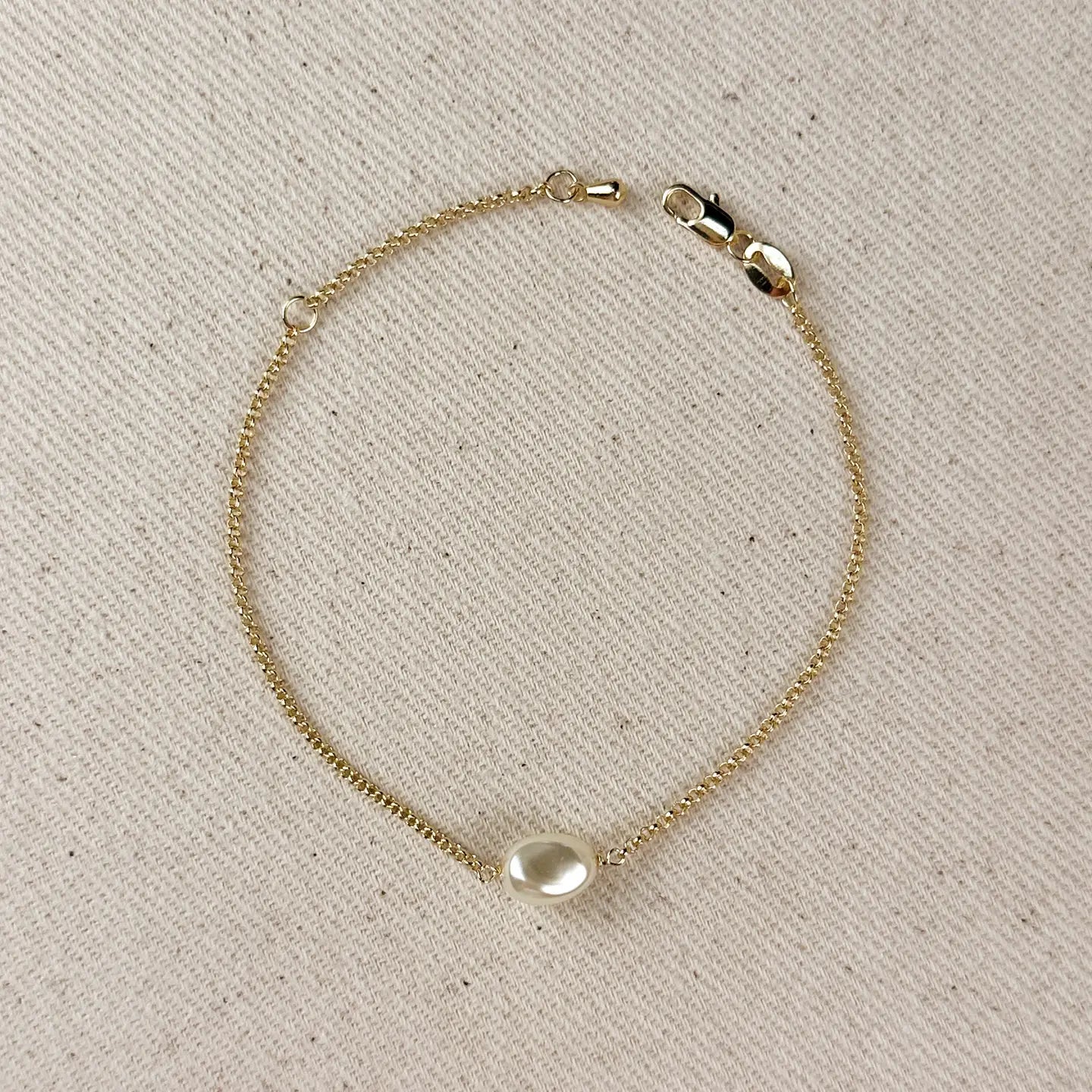 Gold bracelet with a pearl on a beige fabric background