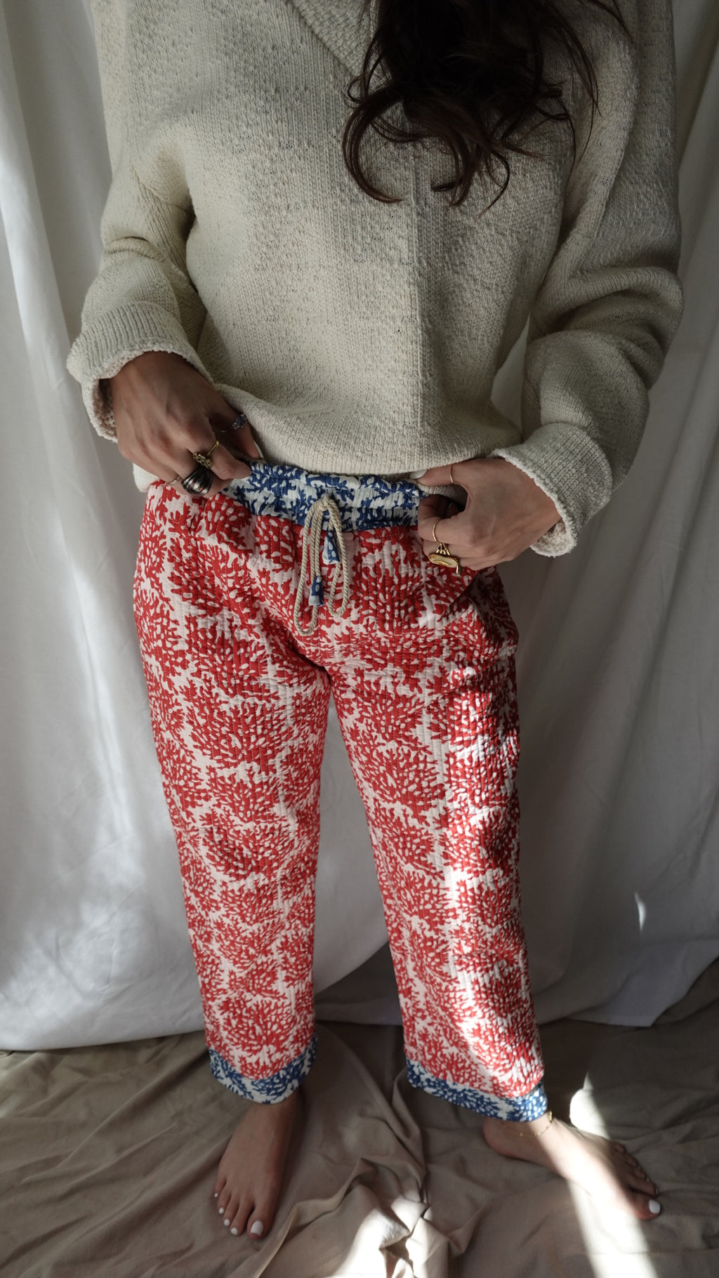 Person wearing red patterned pajama pants sitting on a bed.