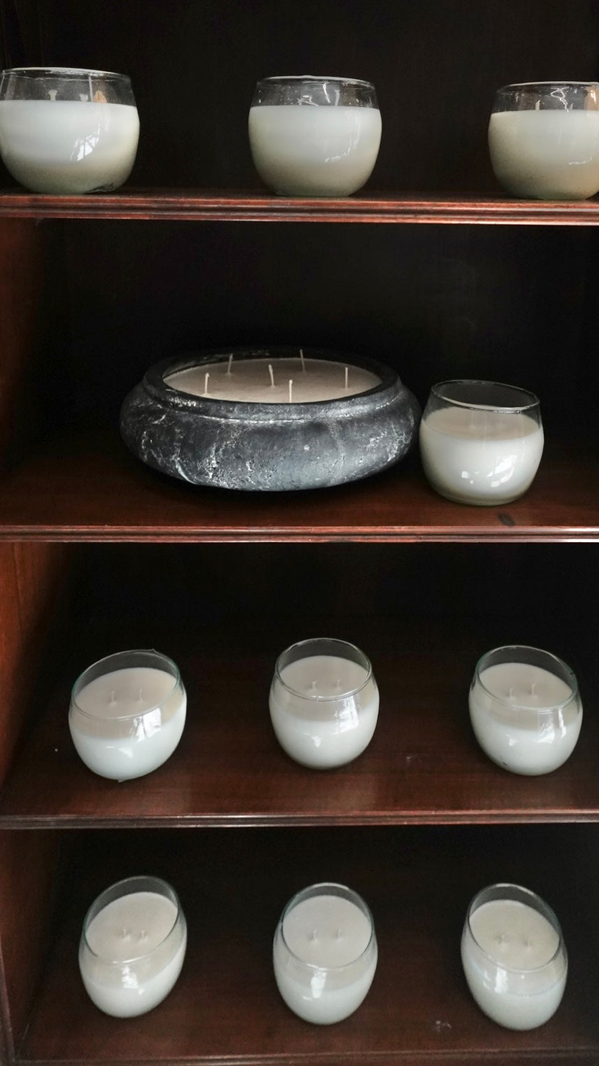 Candles in glass containers on a wooden shelf against a dark background