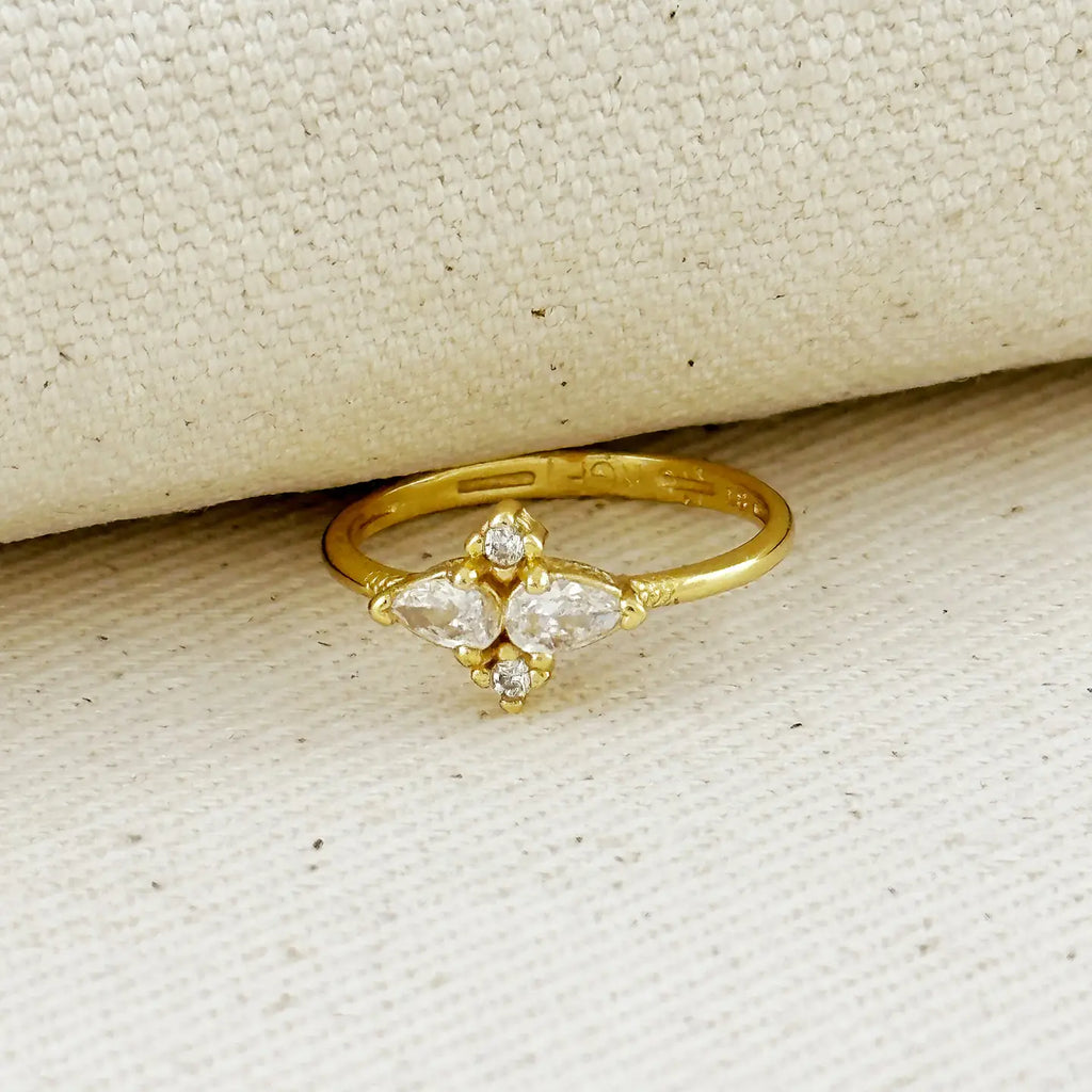 Gold ring with three pear-shaped diamonds on a beige fabric background