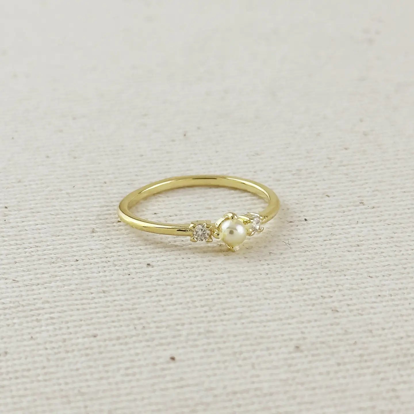 Gold ring with a pearl and small diamonds on a beige fabric background