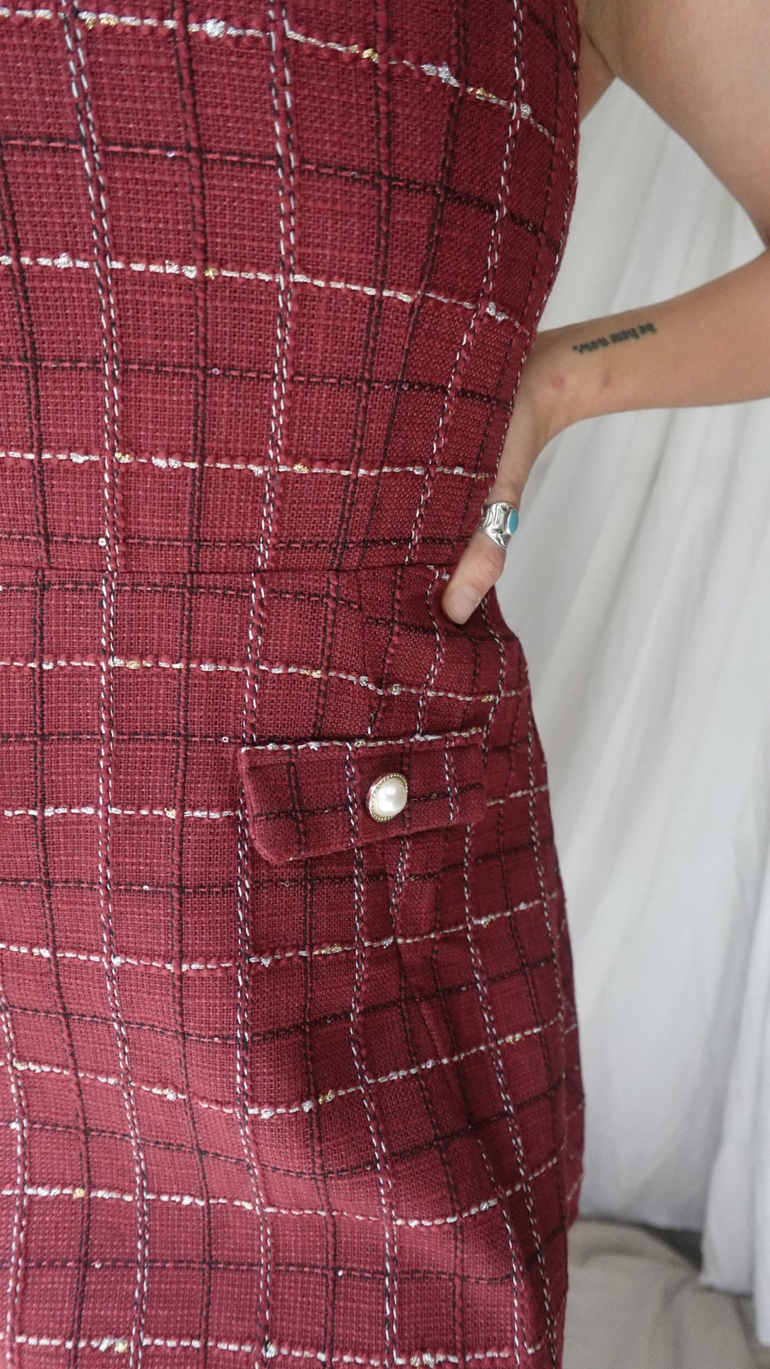Close-up of a red plaid fabric with a button and a person's hand in the background.