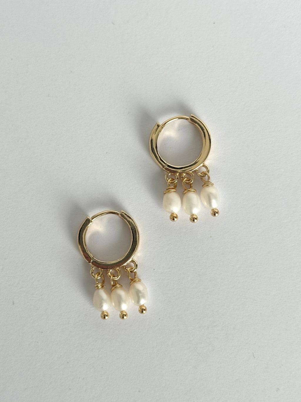 Gold hoop earrings with pearl drops on a light gray background