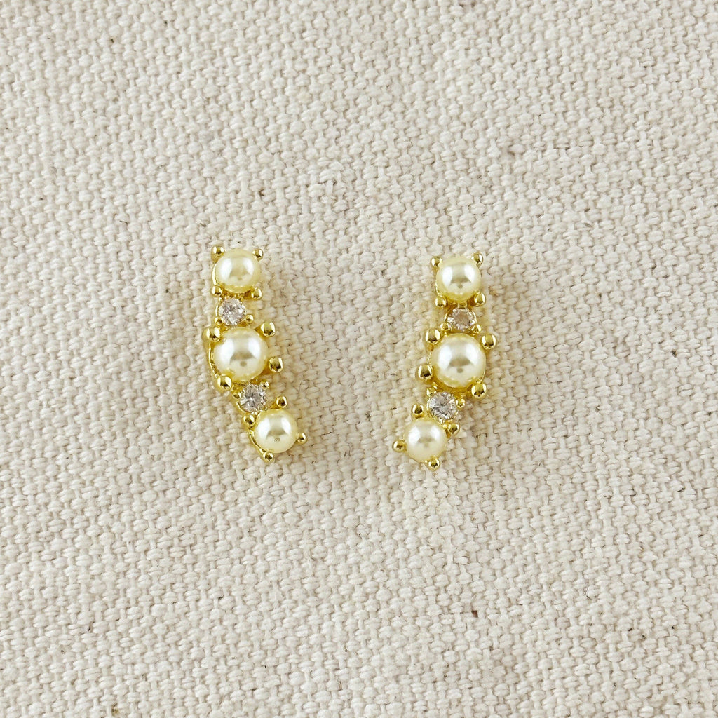 Pair of gold earrings with pearls on a beige fabric background