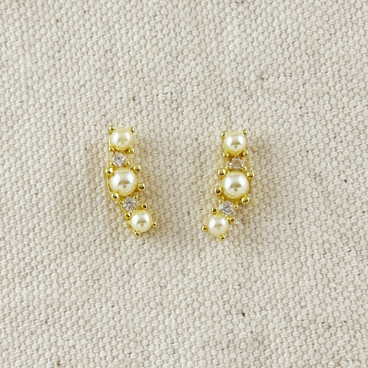 Pair of gold earrings with pearls on a beige fabric background