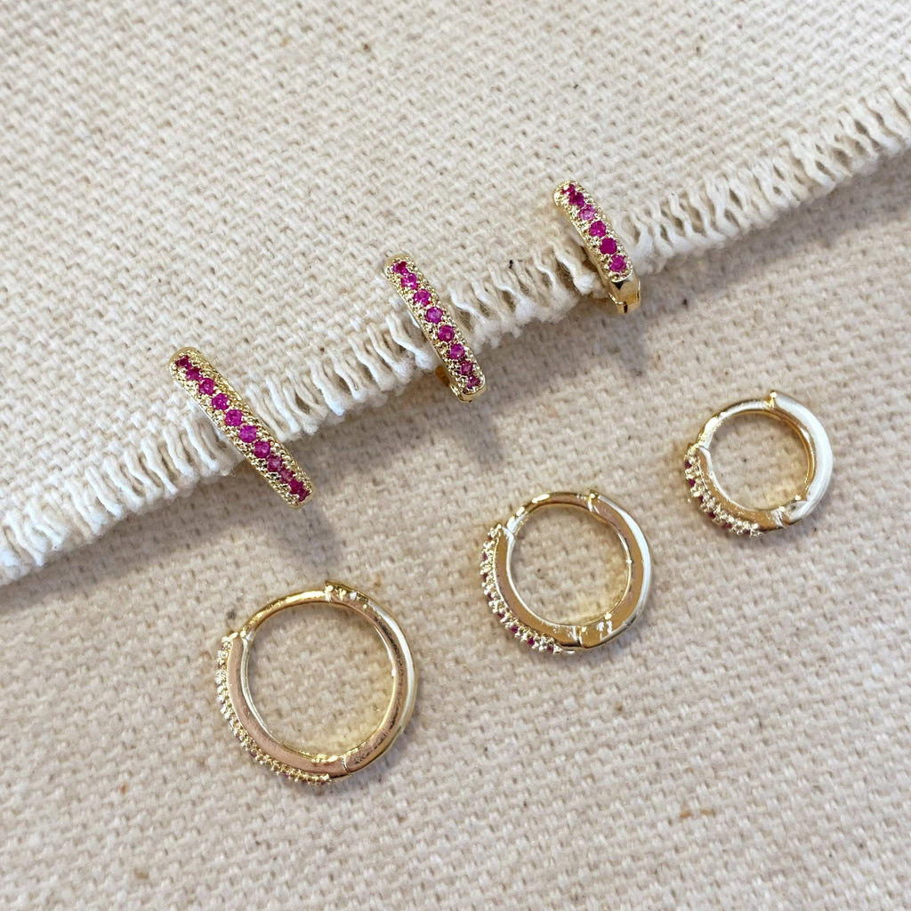 A set of gold-toned hoop earrings with pink gemstone accents, displayed on a textured beige fabric background.