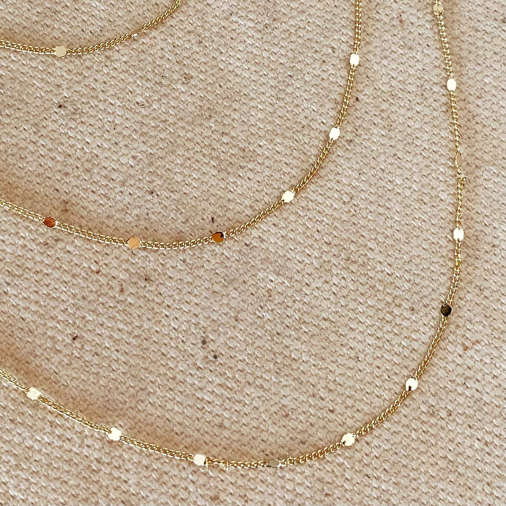 Two gold necklaces with small beads on a beige fabric background