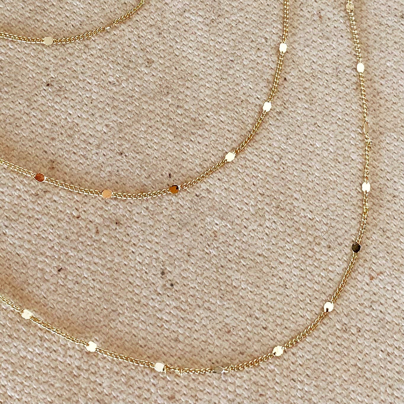 Two gold necklaces with small beads on a beige fabric background