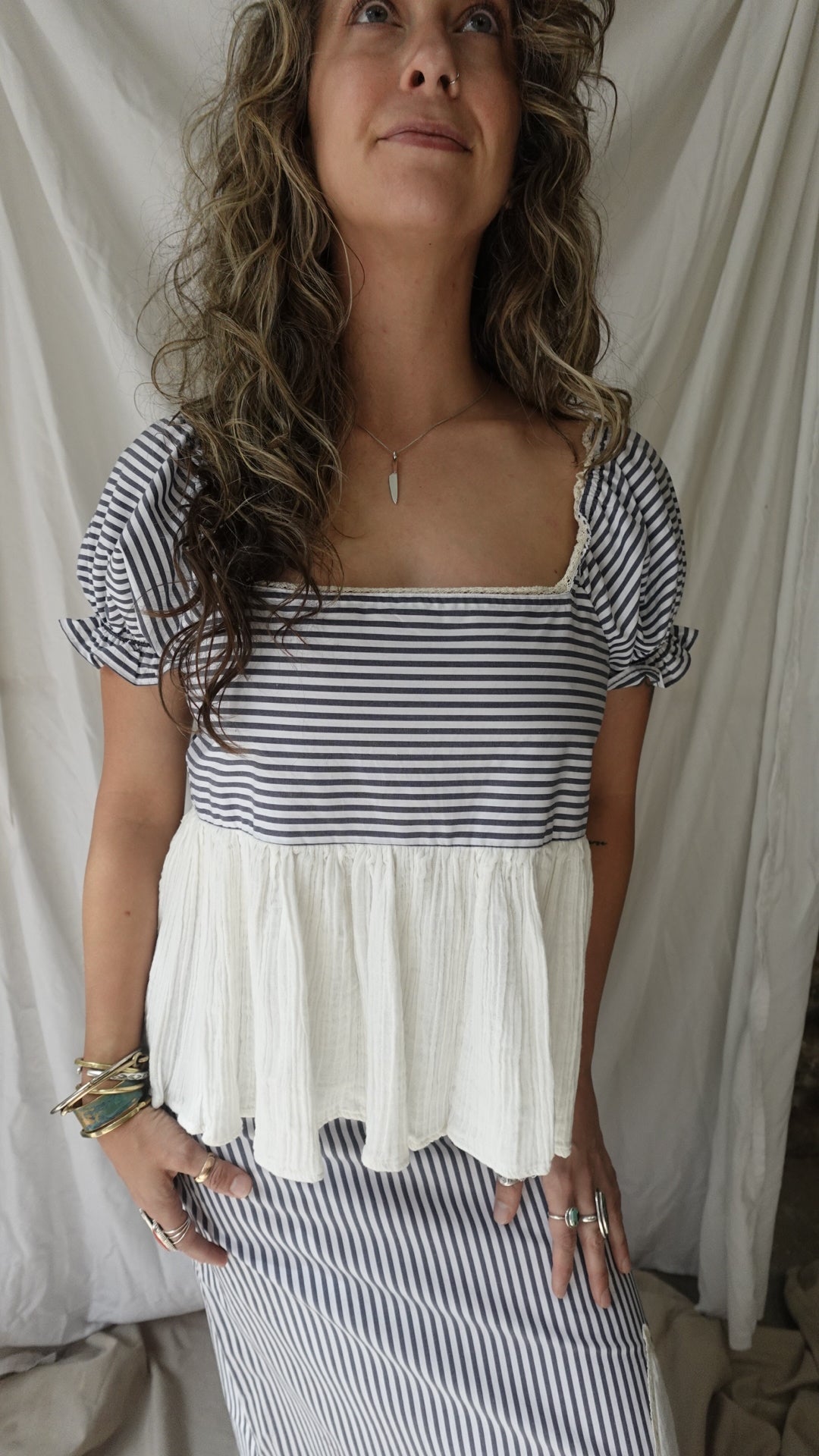 Woman wearing a black and white striped top and pleated skirt against a neutral background