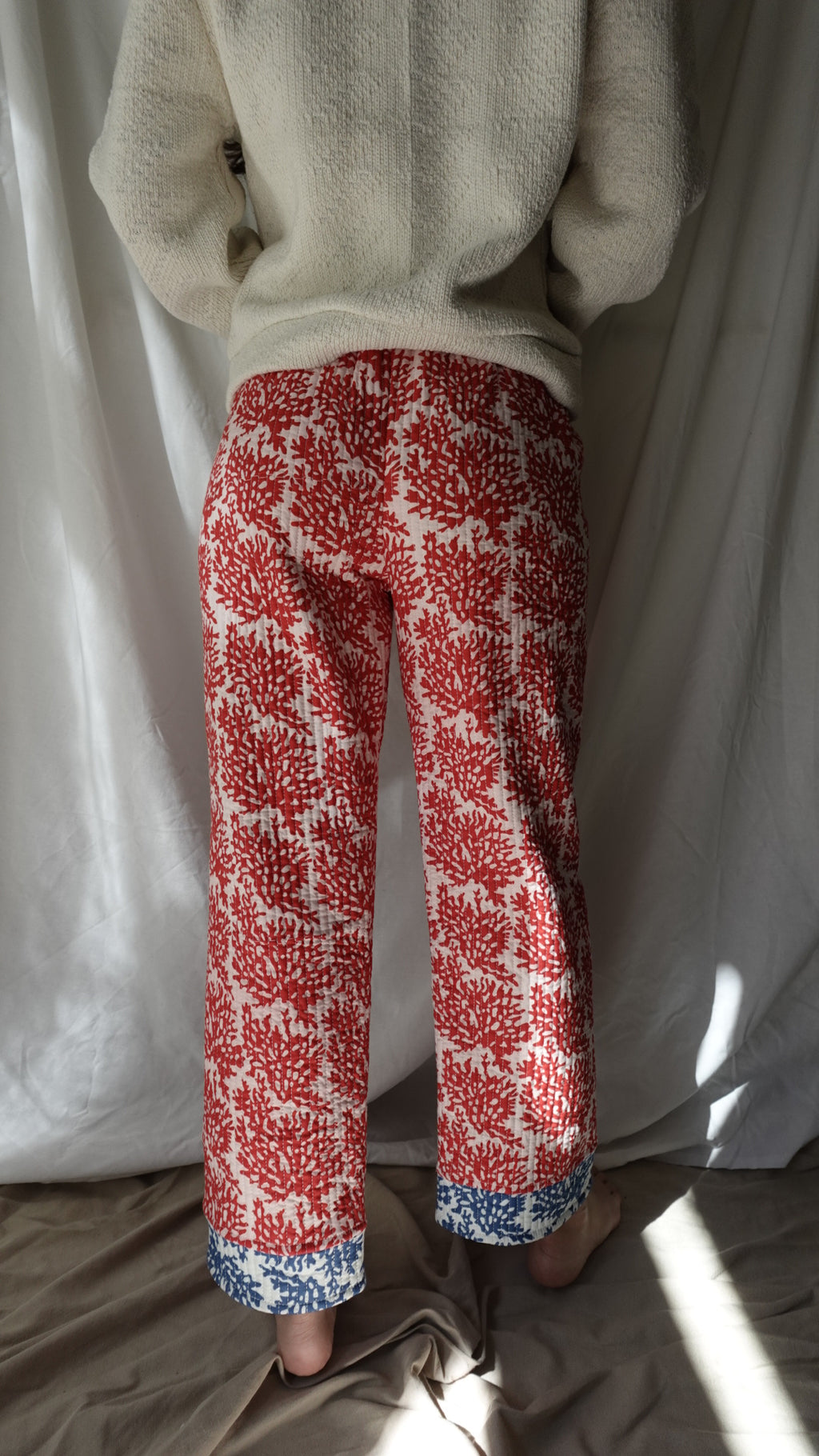 Red and white patterned sleeves with blue cuffs held by a person wearing beige gloves.