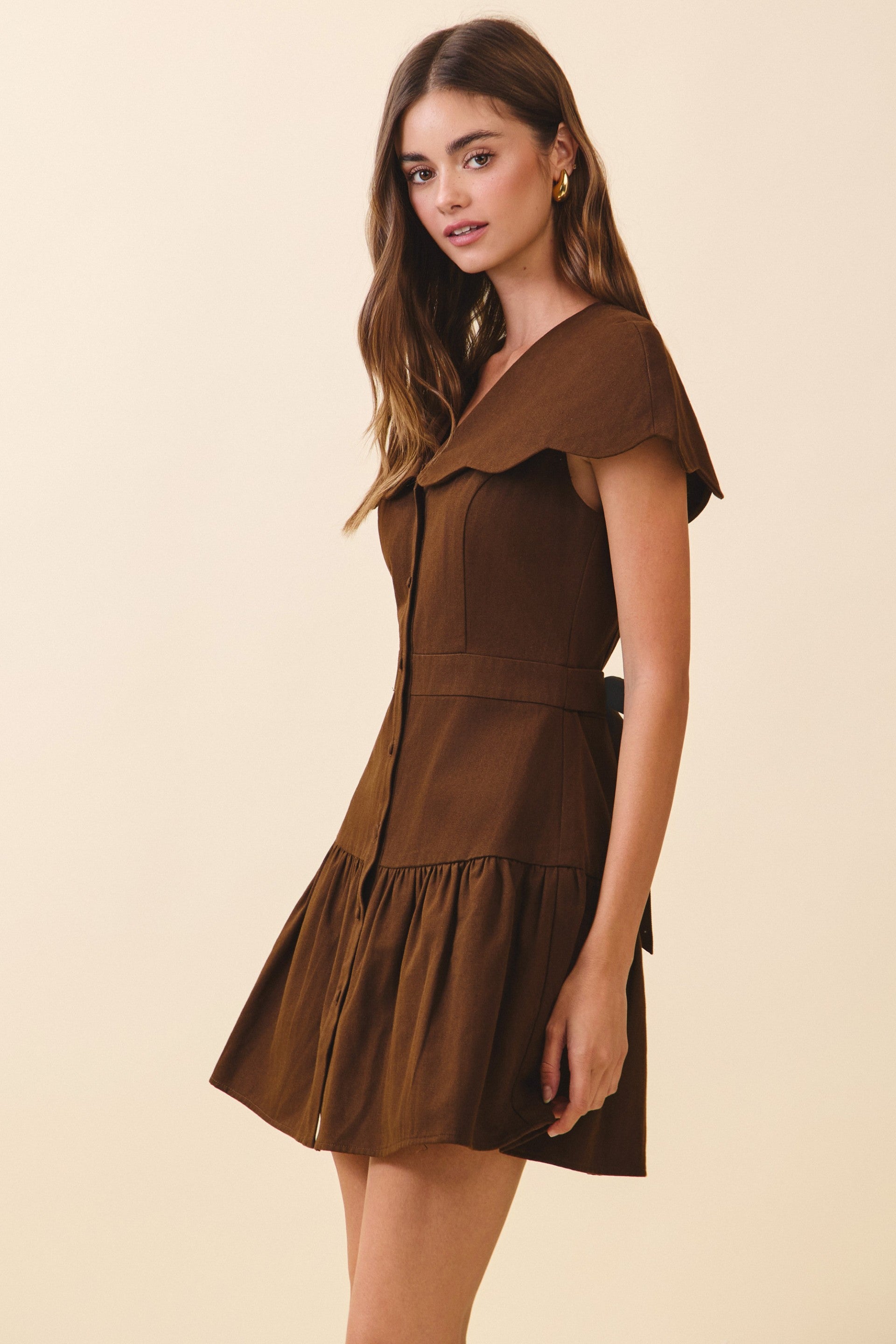 Woman wearing a brown dress with a ruffled collar on a beige background