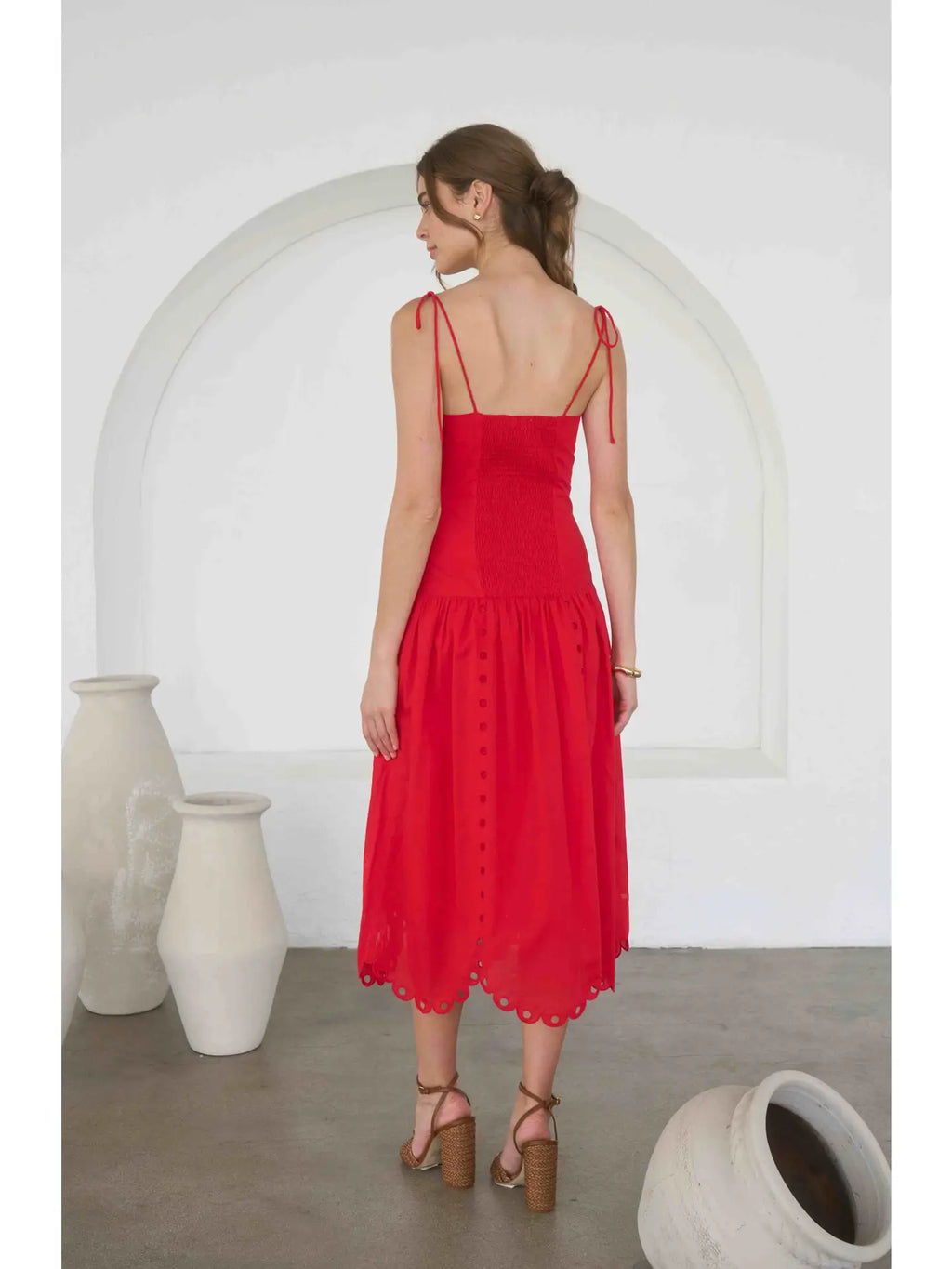 Woman wearing a red dress standing in a minimalistic room with white arches and vases.