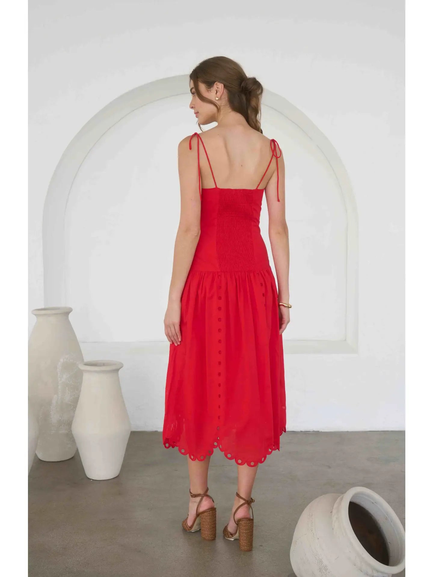 Woman wearing a red dress standing in a minimalistic room with white arches and vases.