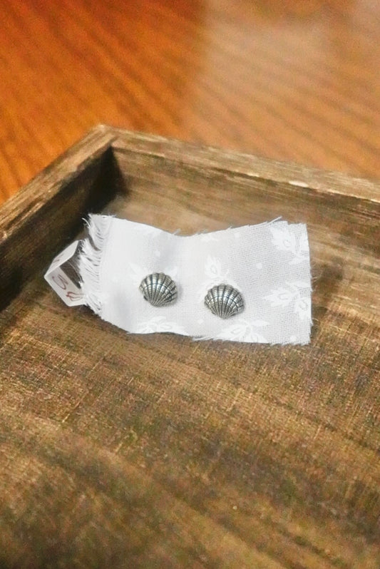 Pair of silver shell earrings on a white card with a wooden surface background