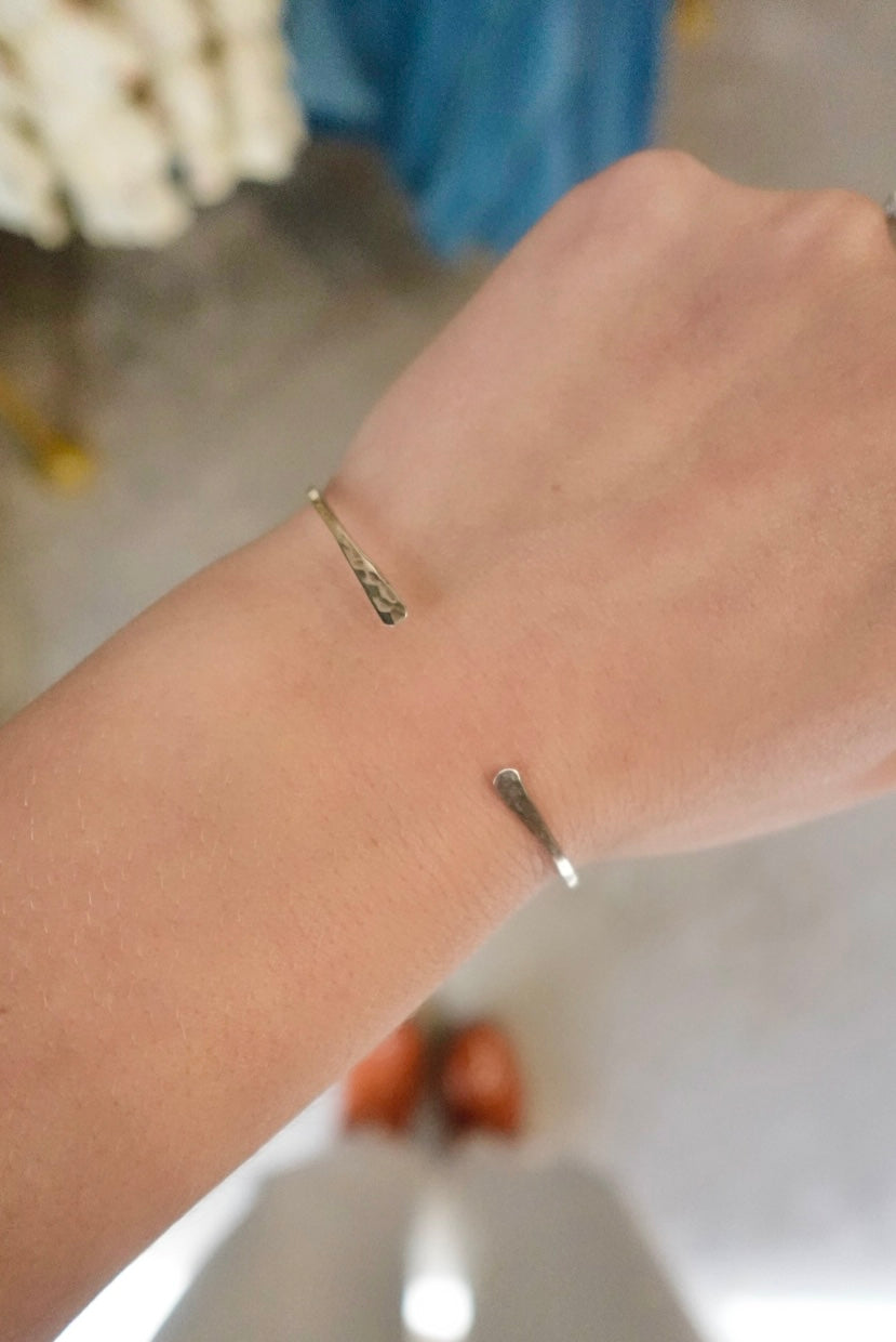 Close-up of a wrist wearing two gold bracelets with a blurred background.